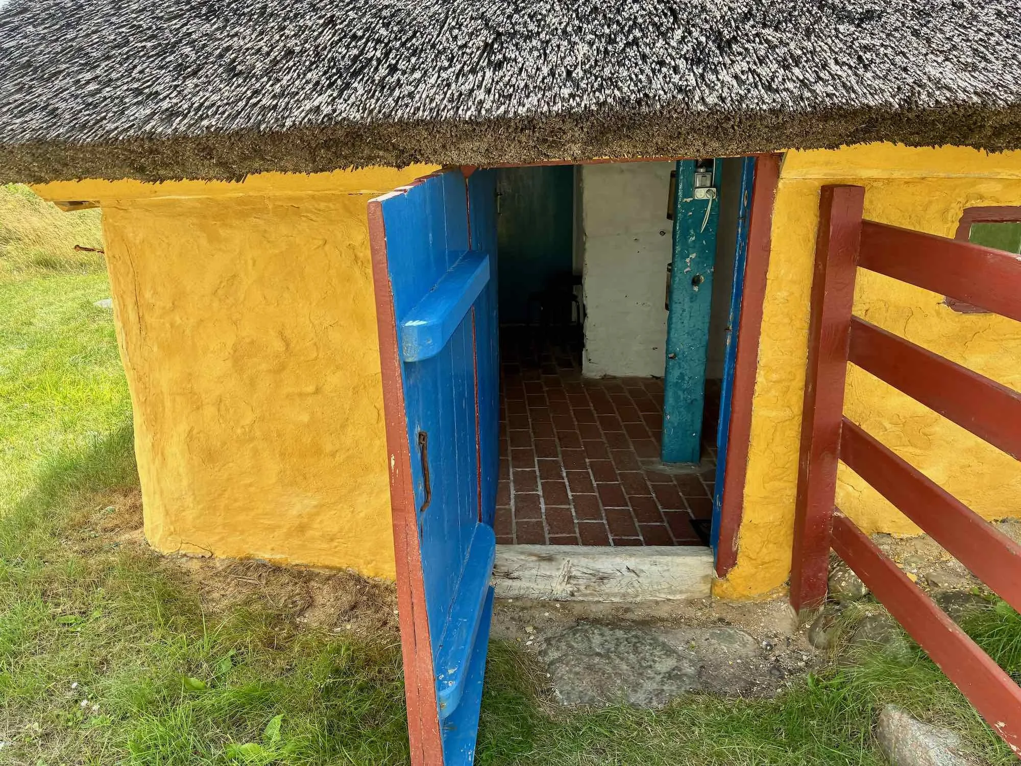 Små træhus med gult væg og blå dør, beliggende i naturskønne omgivelser.