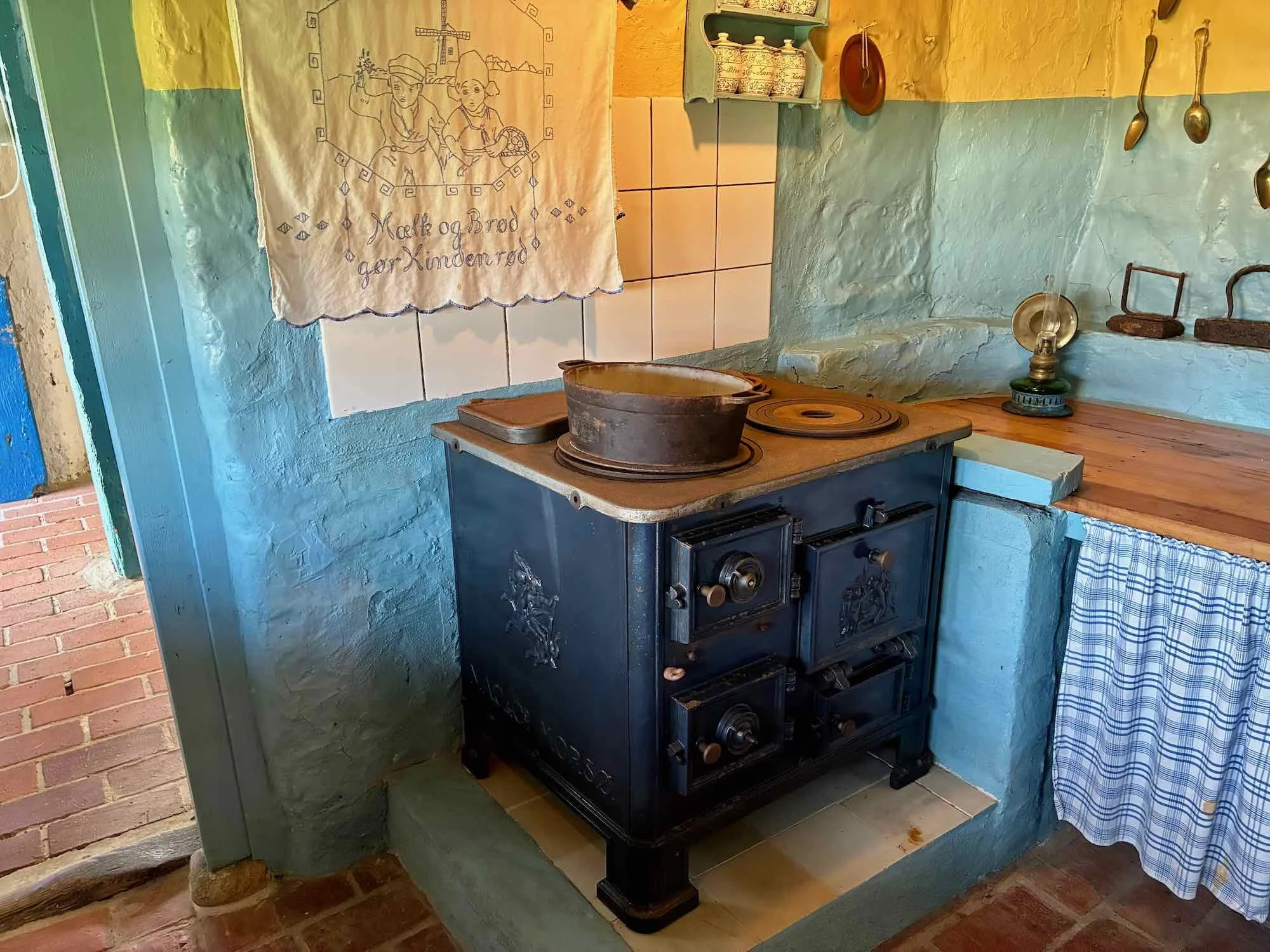 Antik komfur i et køkken med farvede vægge, kobbergryder og gammeldags lamper.