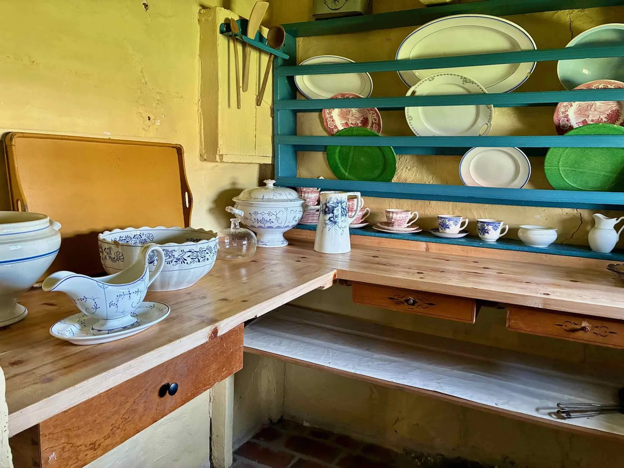 Køkkenskab med porcelænsservice og skærebræt. Opbevaringshylder med tallerkener og kopper. Vintage køkkentilbehør.