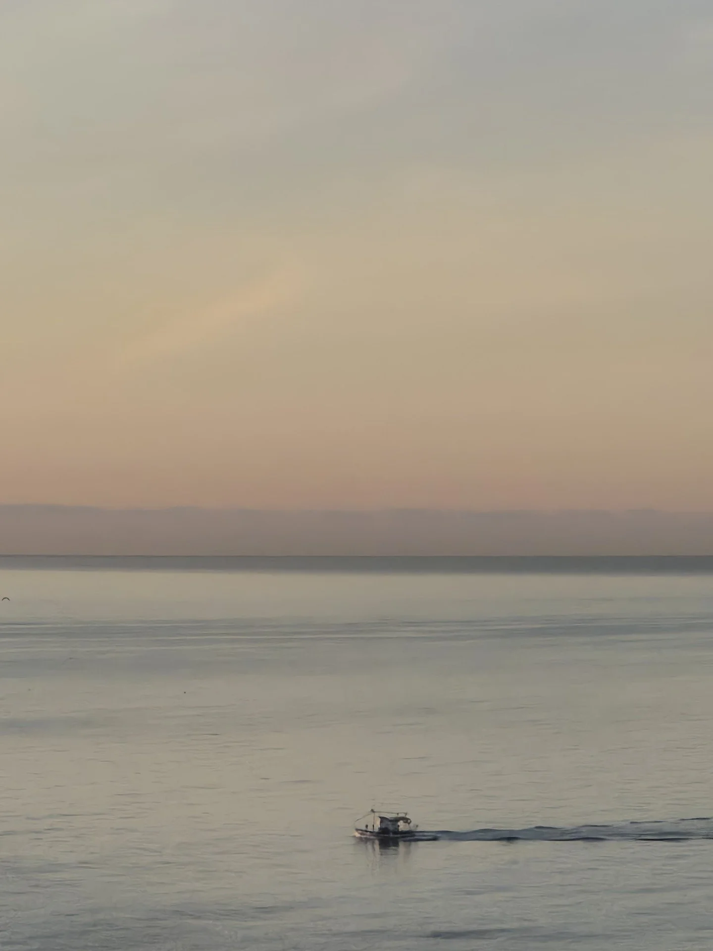 Hiljainen meri auringonlaskun aikaan, pieni vene liikkuu vedessä.