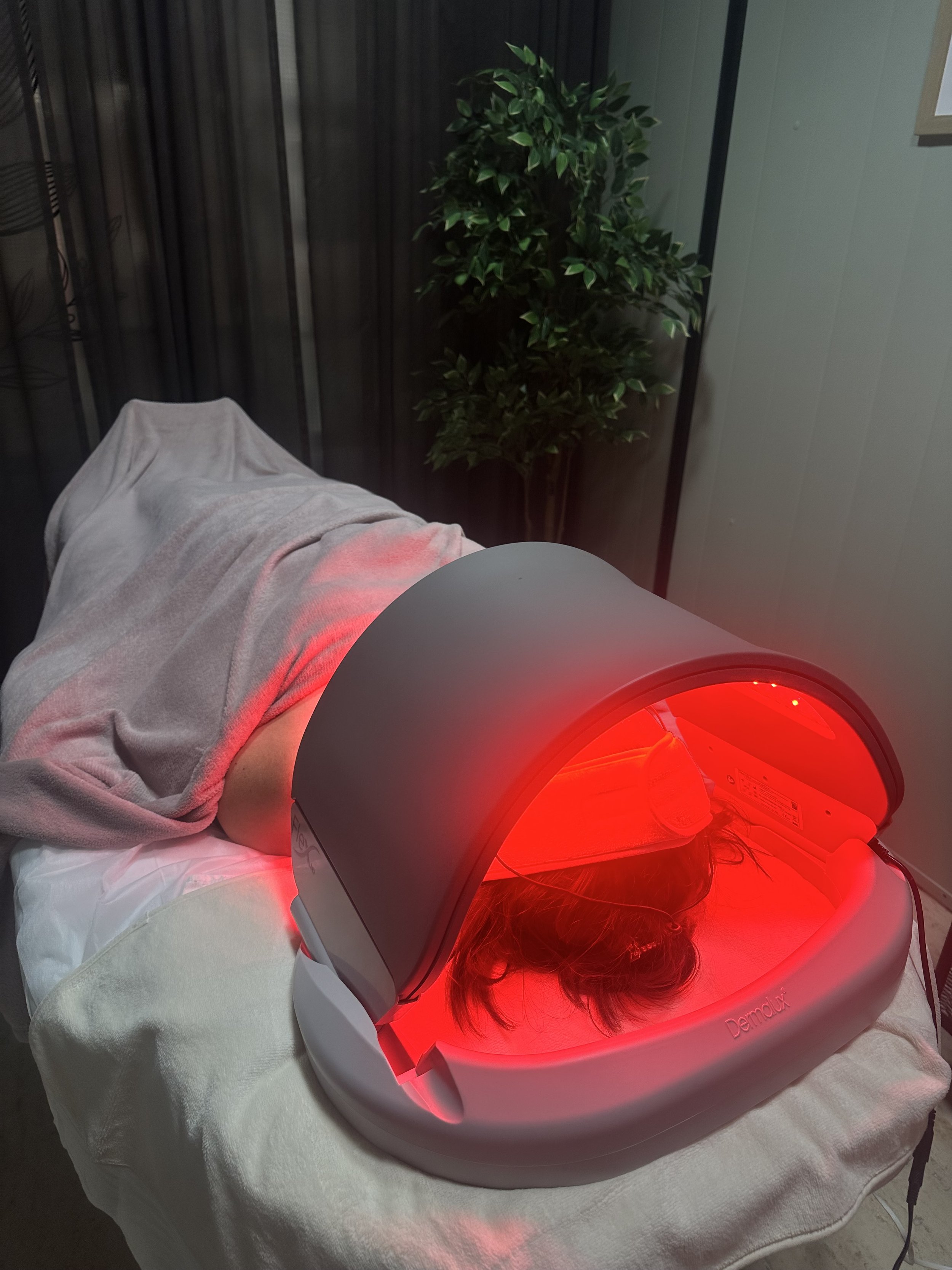 The client lies on the treatment table and receives light therapy from a red device