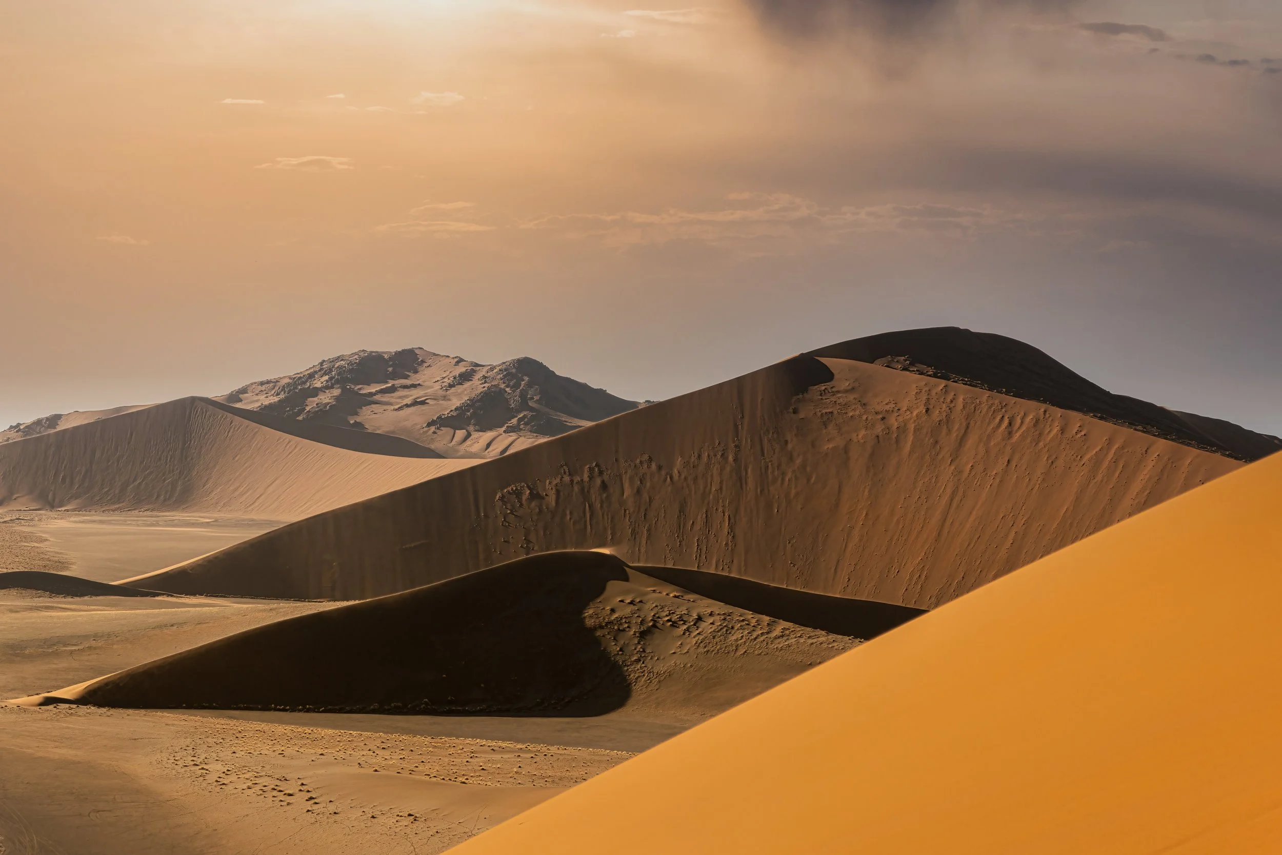 Sand dunes in a desert under a partly cloudy sky with more sand dunes in the distance. Namib desert. Namibia.