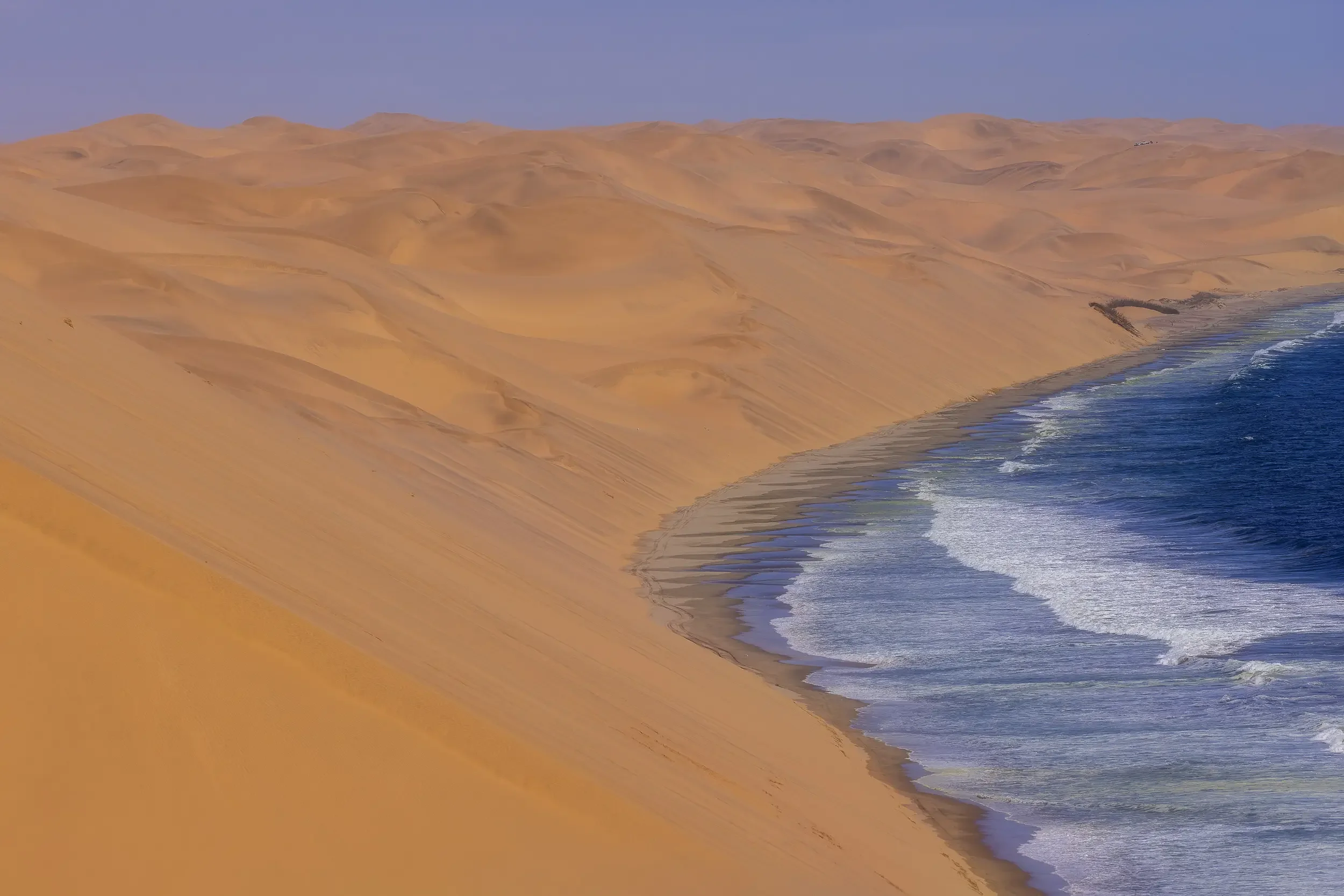 Sand dunes meeting the ocean with waves along the shoreline.