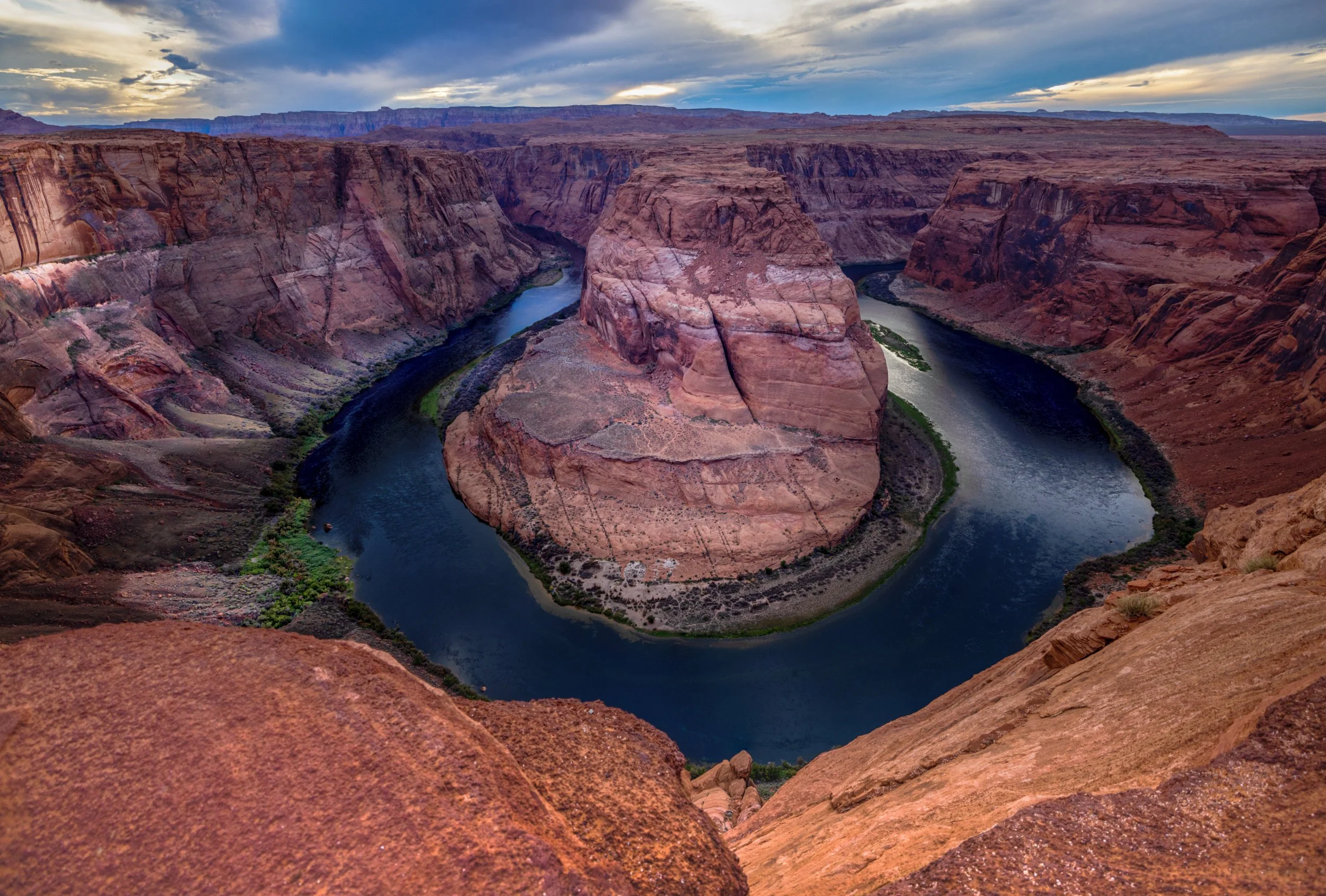 A wide view of Horseshoe Bend, a meander in the Colorado River, surrounded by red rock cliffs in the desert.