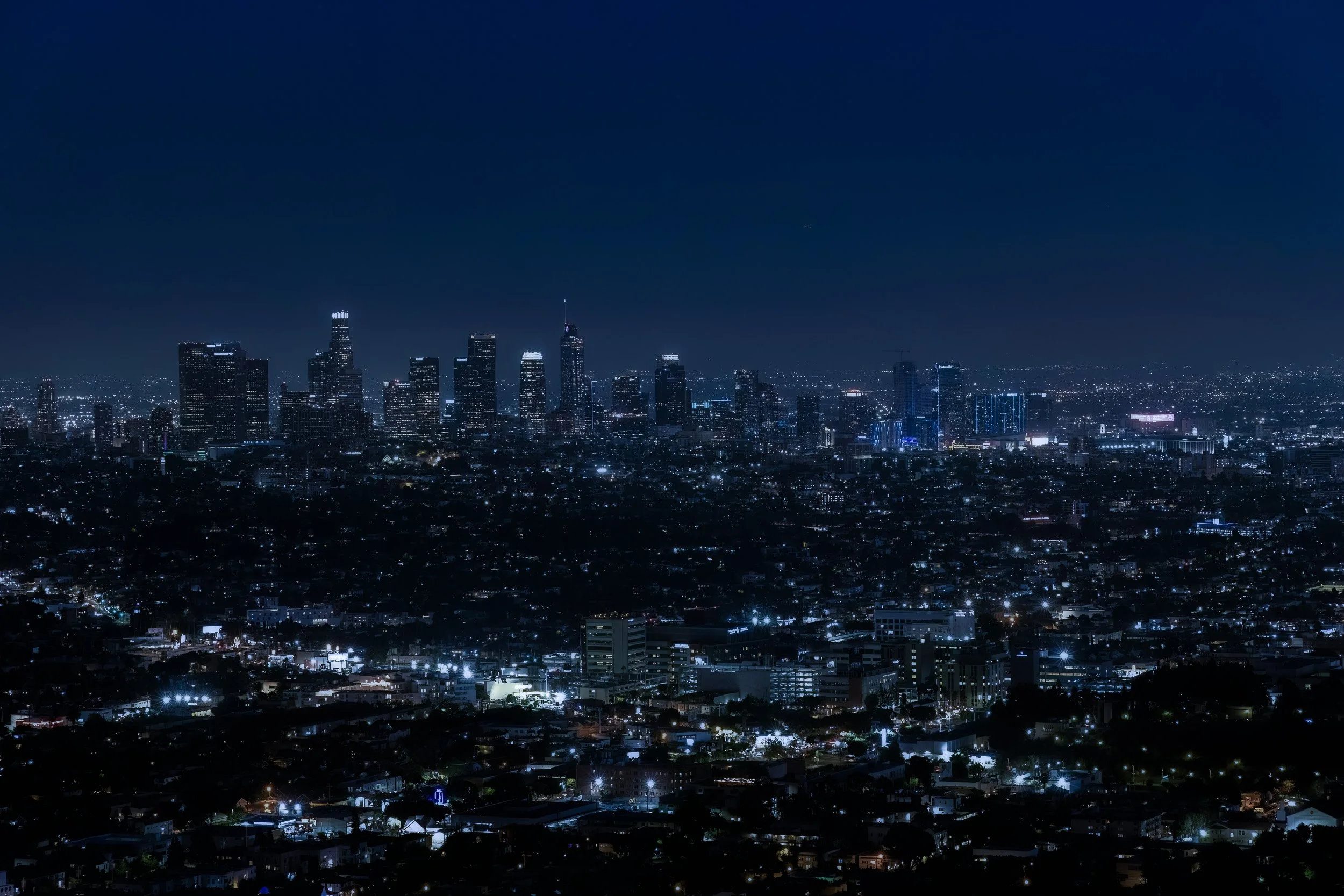 Nighttime city skyline with tall illuminated skyscrapers and many smaller city lights in Los Angeles.