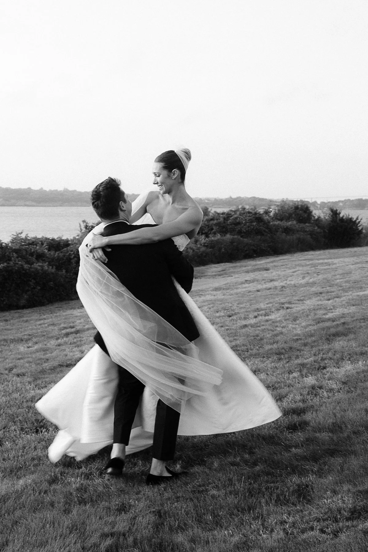 black and white image of groom spinning bride on lawn with veil flowing