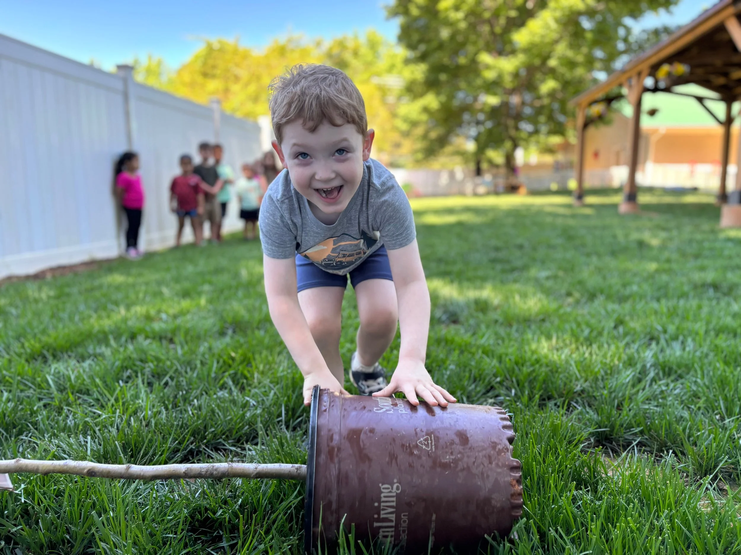 Two preschool aged boys playing outside with green grass and trees in the background.