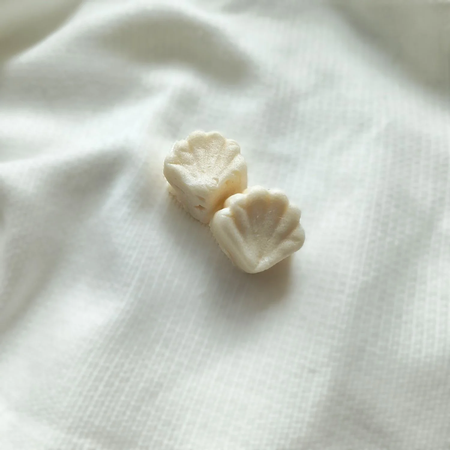 Set of two Cashmere Cream Sugar Balm Shells pictured on textured background.