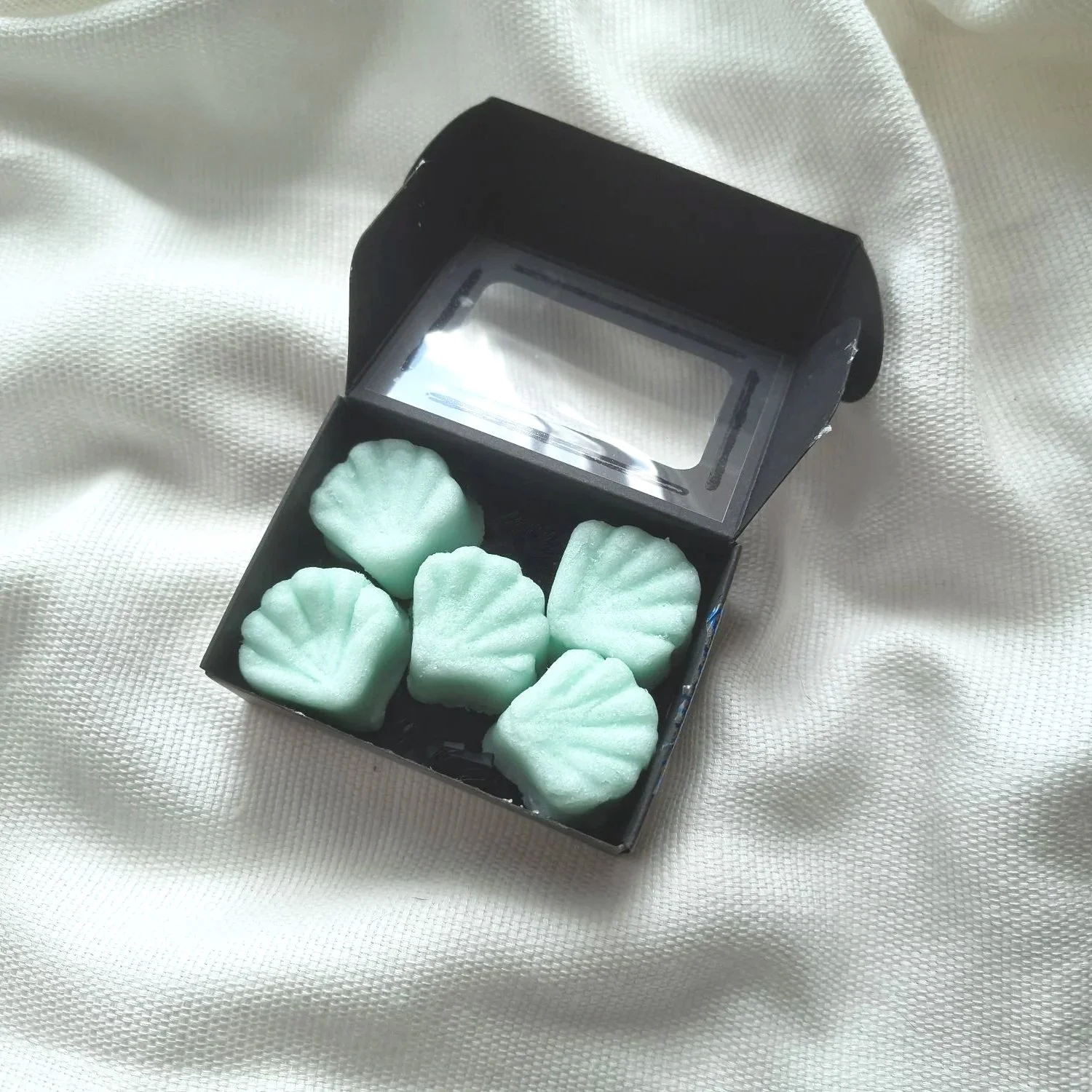 Set of five blue colored, shell shaped Pineapple Sorbet Sugar Balm Shells in black box on textured cream background.