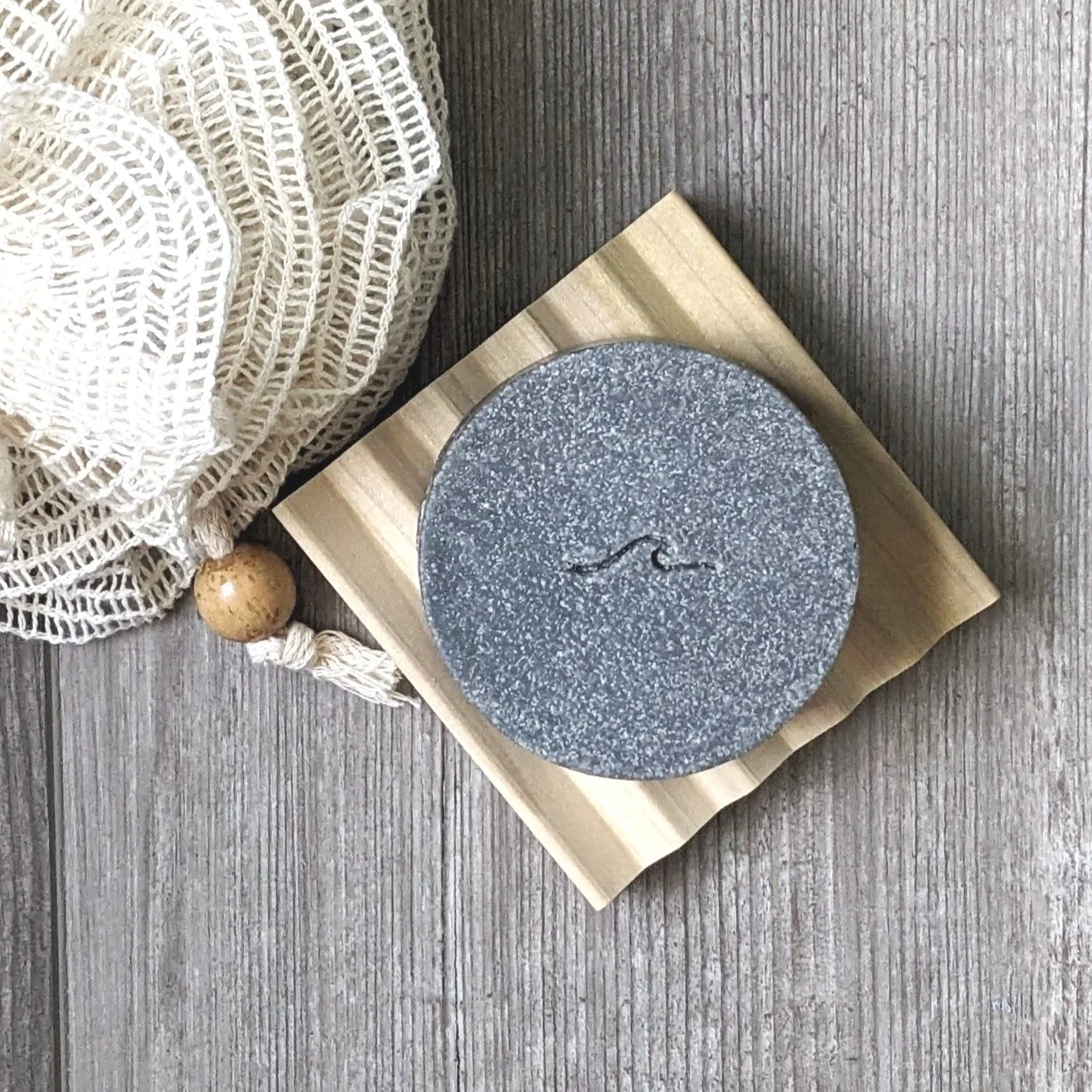Round charcoal infused sea salt soap bar on natural wood soap dish, cedar and oud scented soap for men.