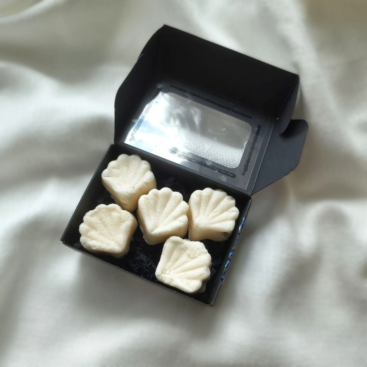 Set of five Cashmere Creme Sugar Balm Shells, pictured on black box on textured cream colored background.