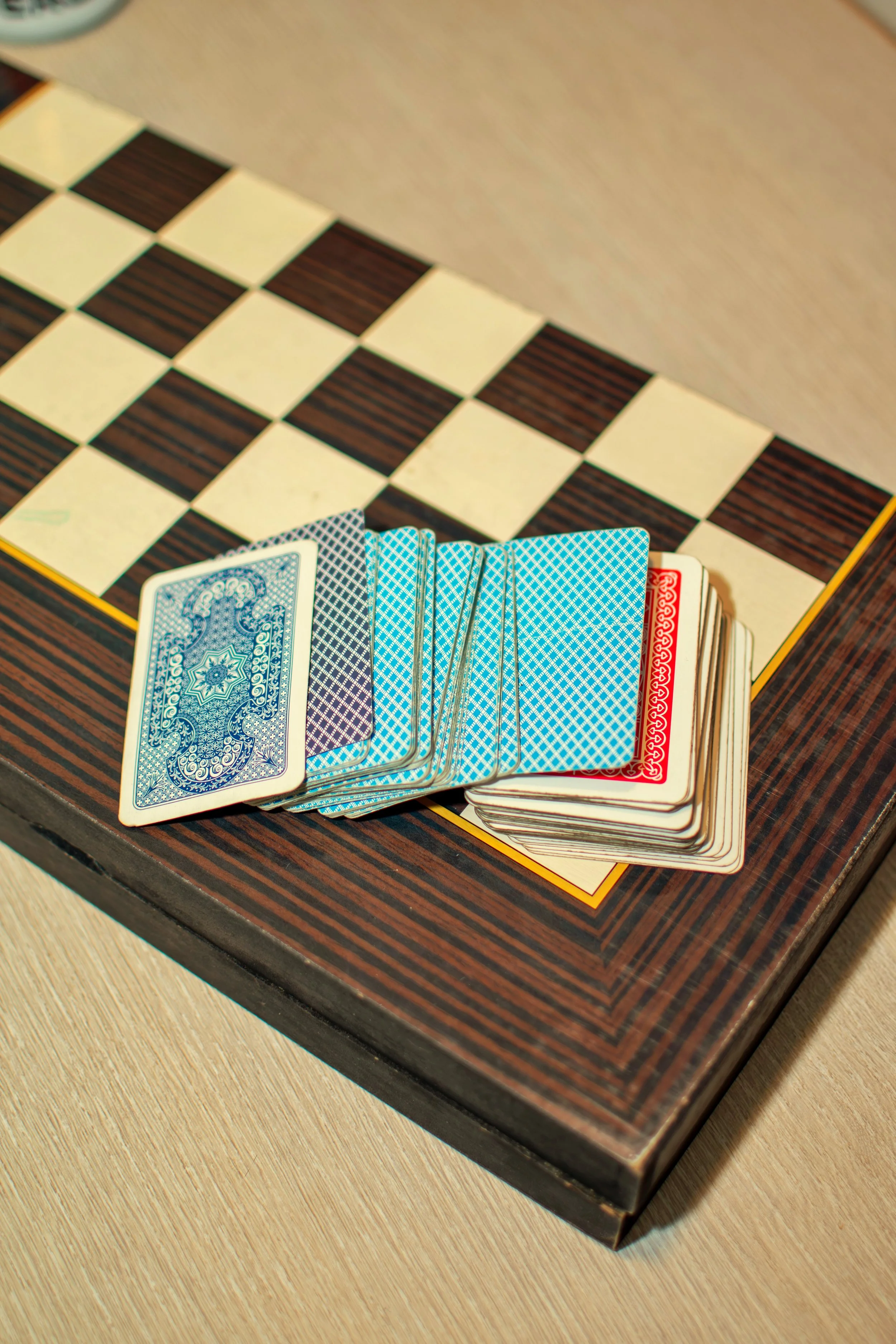 A set of playing cards on a chessboard, with the cards arranged face down in a fan shape, showing their blue and red patterned backs.