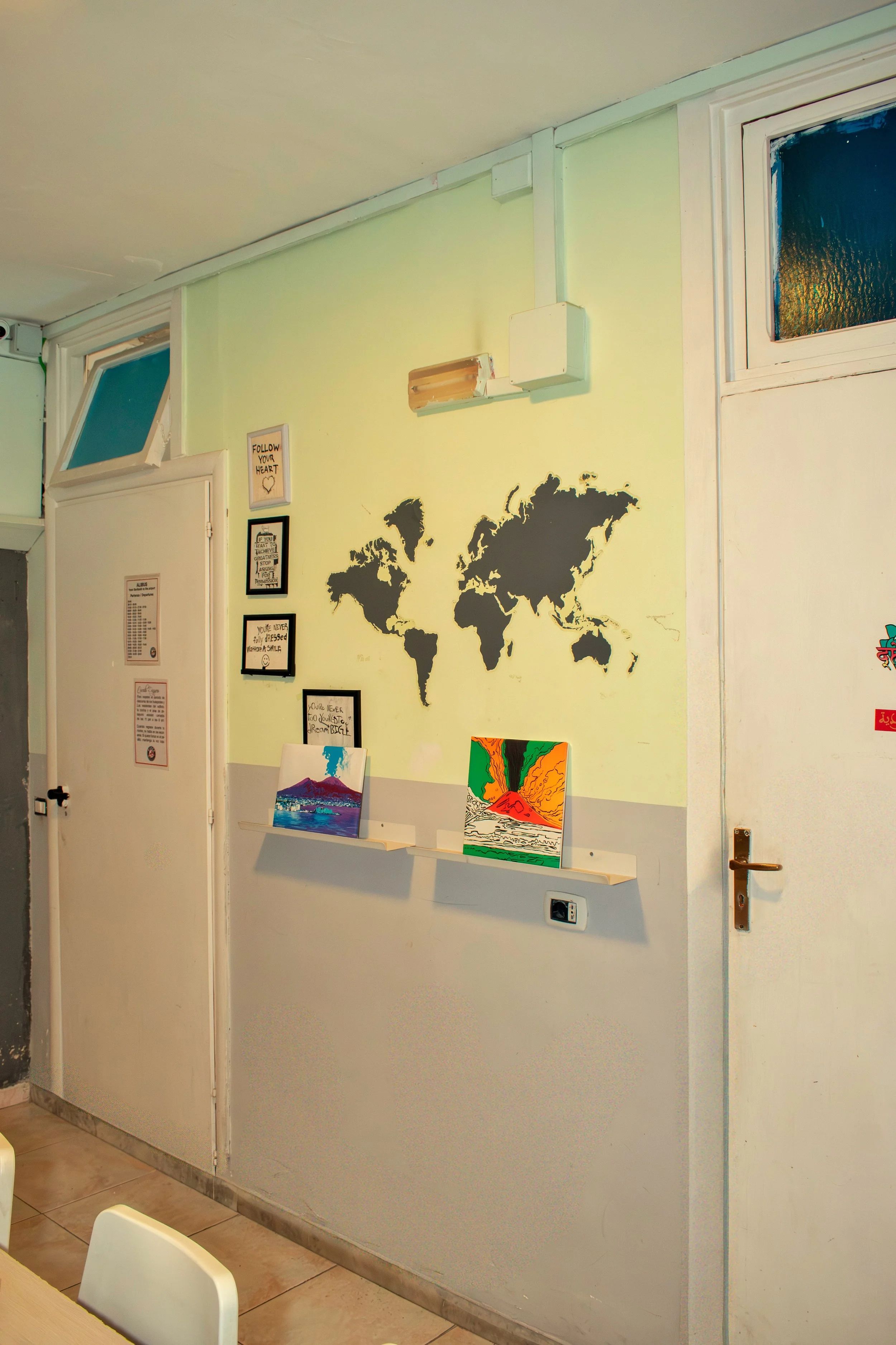 Interior wall with a world map decal, framed quotes, and two acrylic paintings of volcanoes on a shelf.