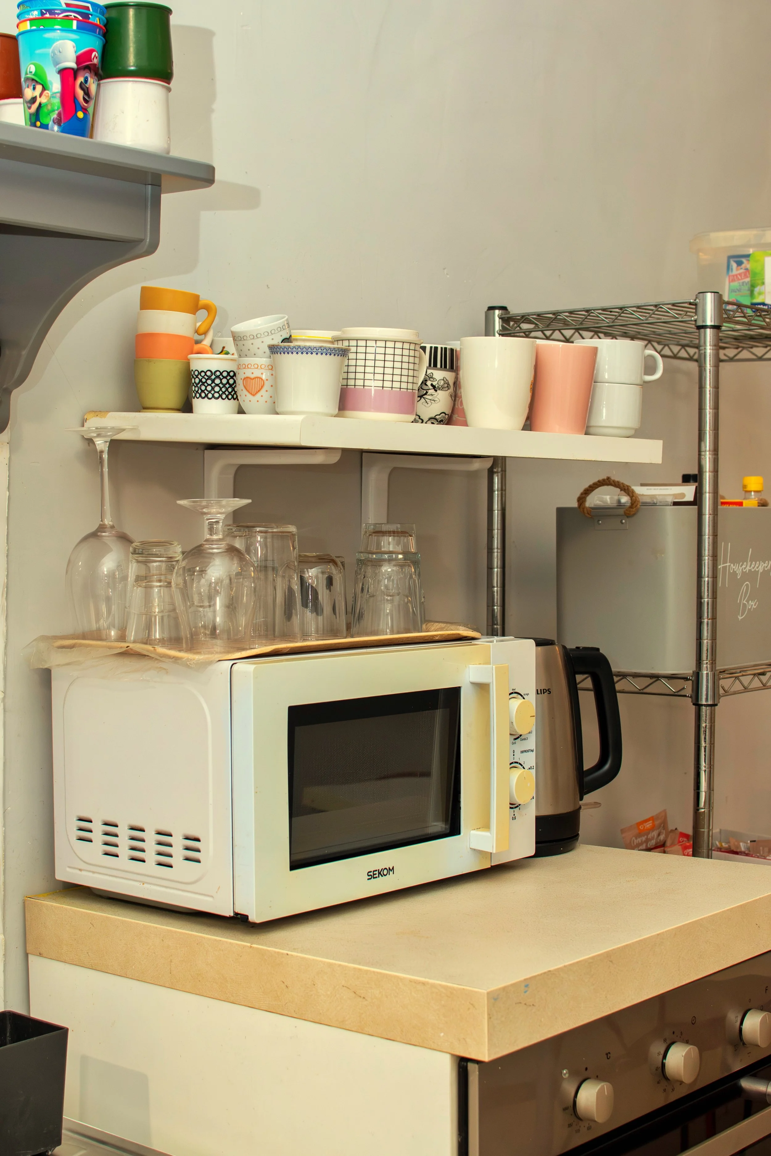 Kitchen shelf with cups and glasses, microwave oven, electric kettle, and countertop in a kitchen setting.