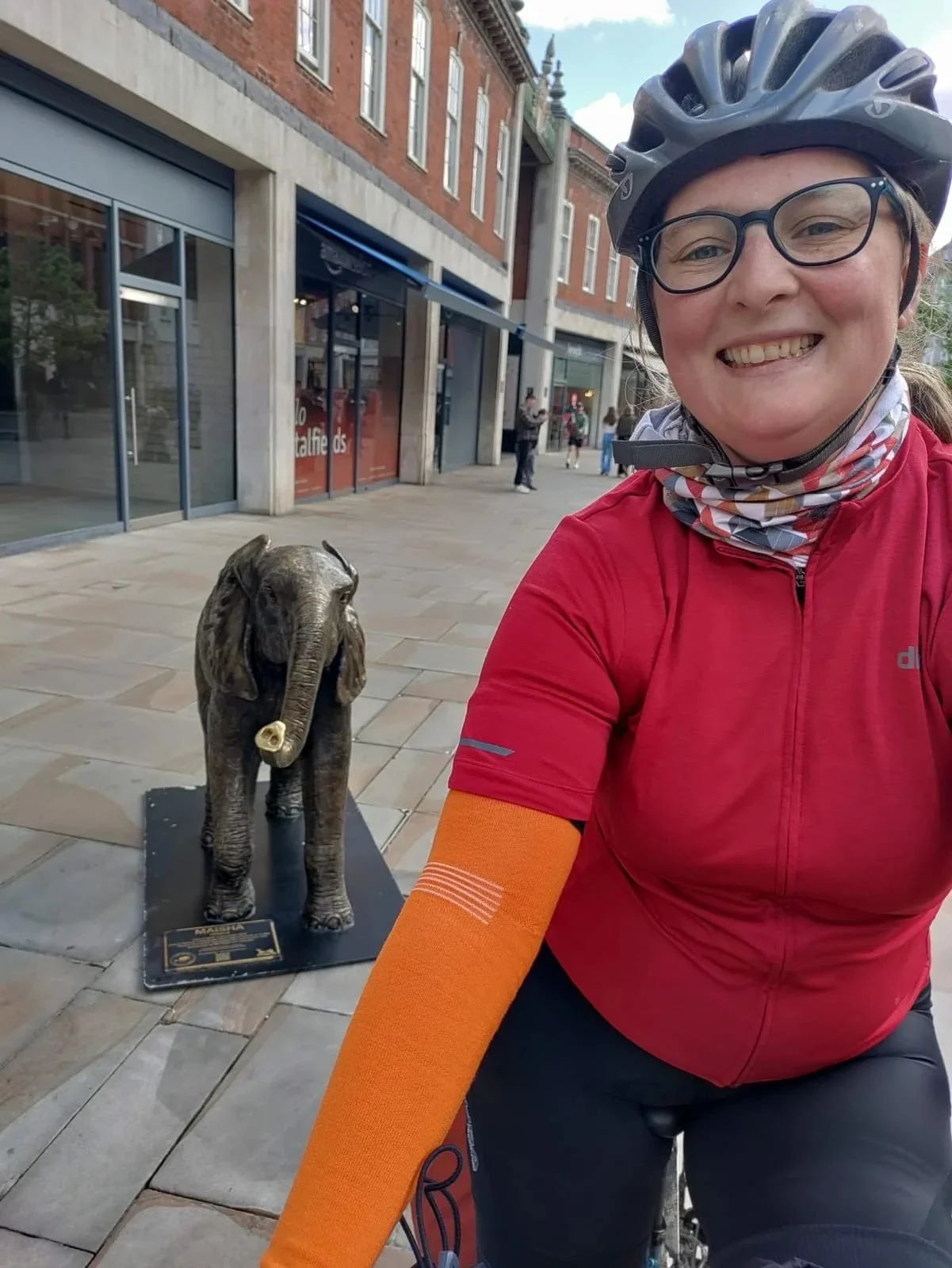 Image shows Megan on a bike next to a sculpture of a baby elephant.