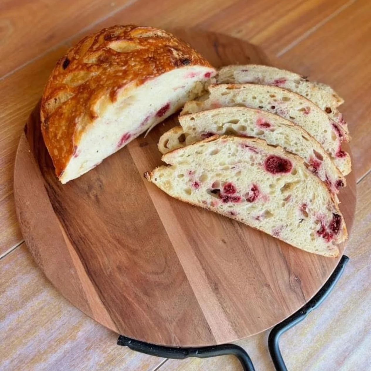 Sliced fruit bread with berries on a round wooden cutting board.