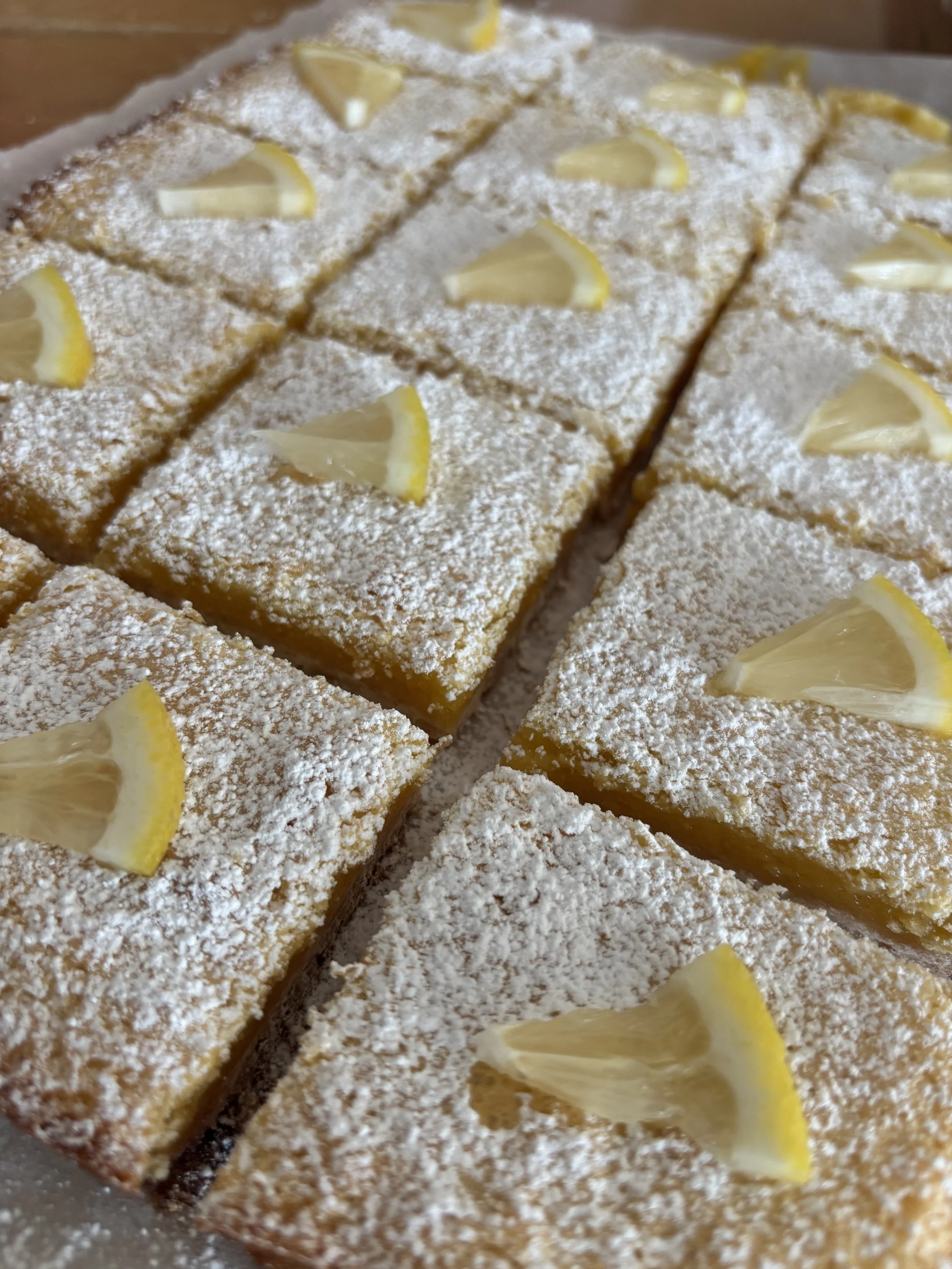 Lemon bars dusted with powdered sugar and garnished with lemon wedges.