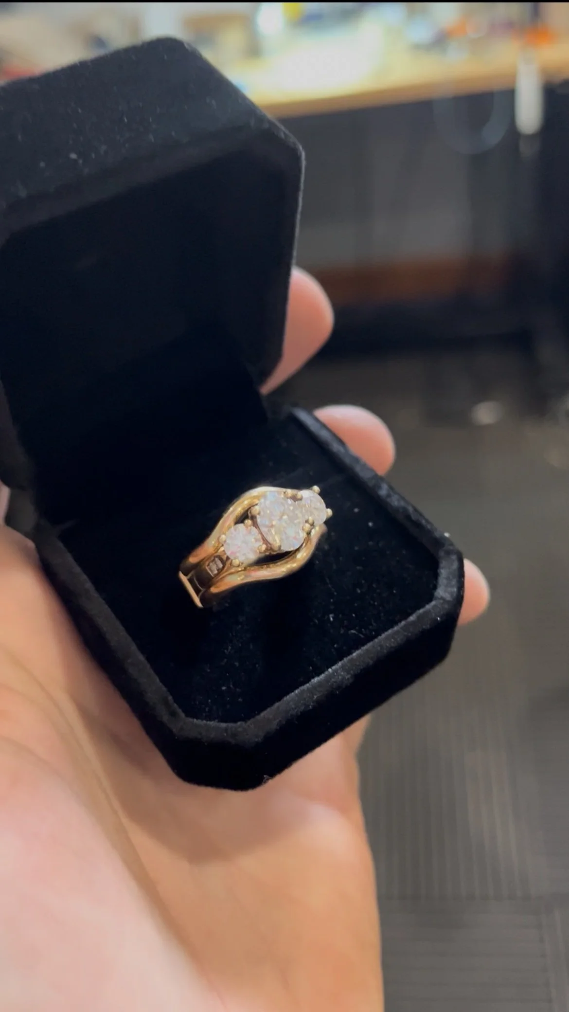 A gold ring with a cluster of diamonds in a black box.