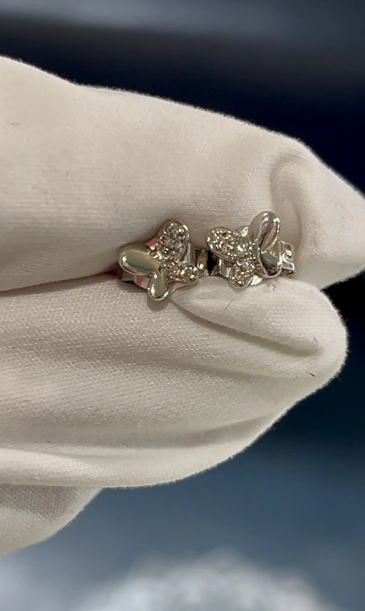 A silver ring with two butterfly-shaped designs, some adorned with small diamonds, is held by a white cloth.