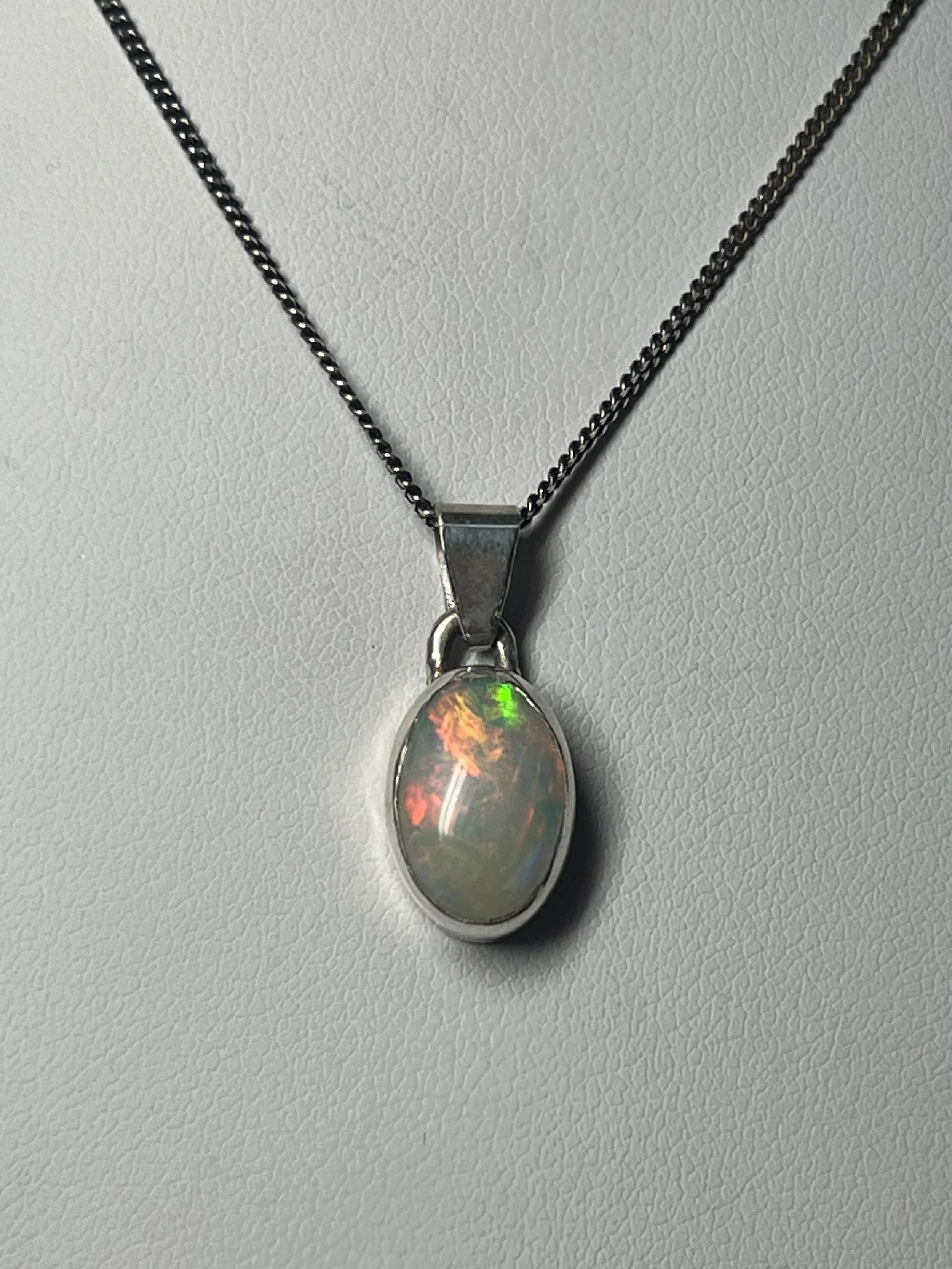 A silver pendant necklace with an oval-shaped opal stone hanging on a silver chain.