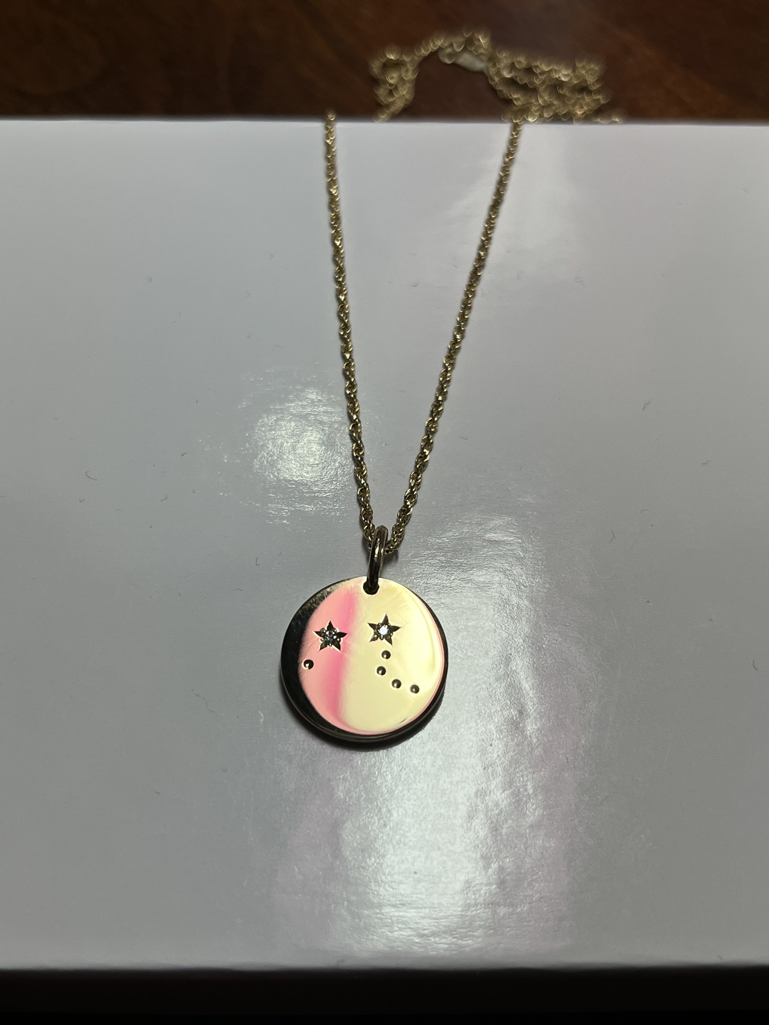 A gold necklace with a round pendant featuring a star-shaped and round-cut diamonds, hanging on a white surface with a brown background.