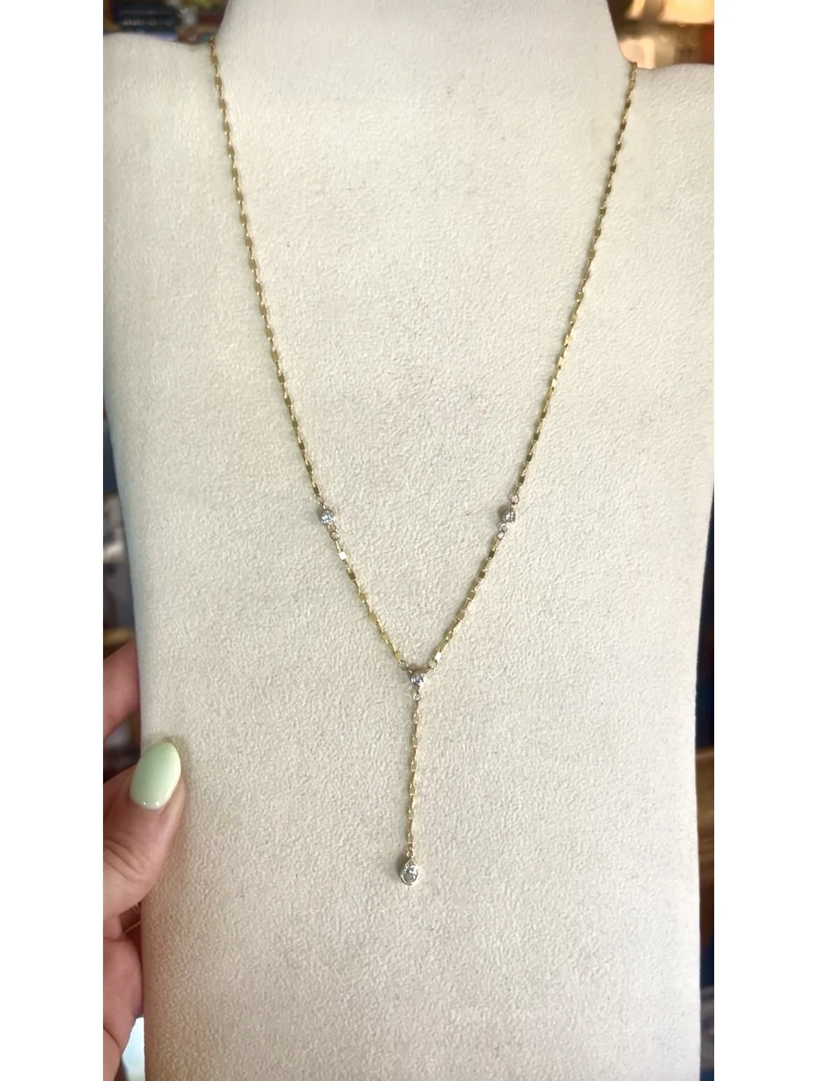 Gold necklace with small diamond accents displayed on a beige jewelry stand.