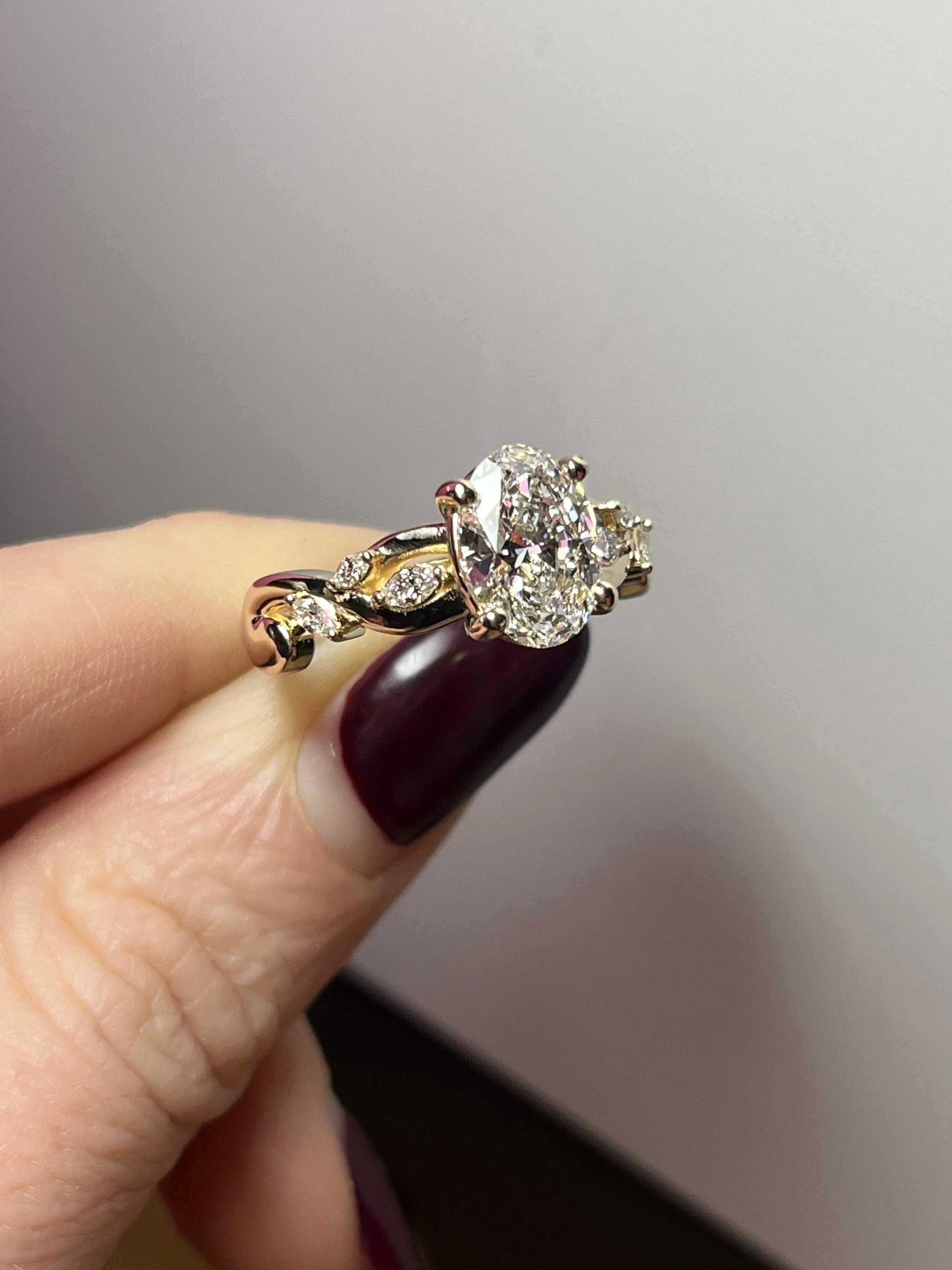 A gorgeous oval engagement ring with a vine-inspired diamond accented band, custom made by TSC Jewelry