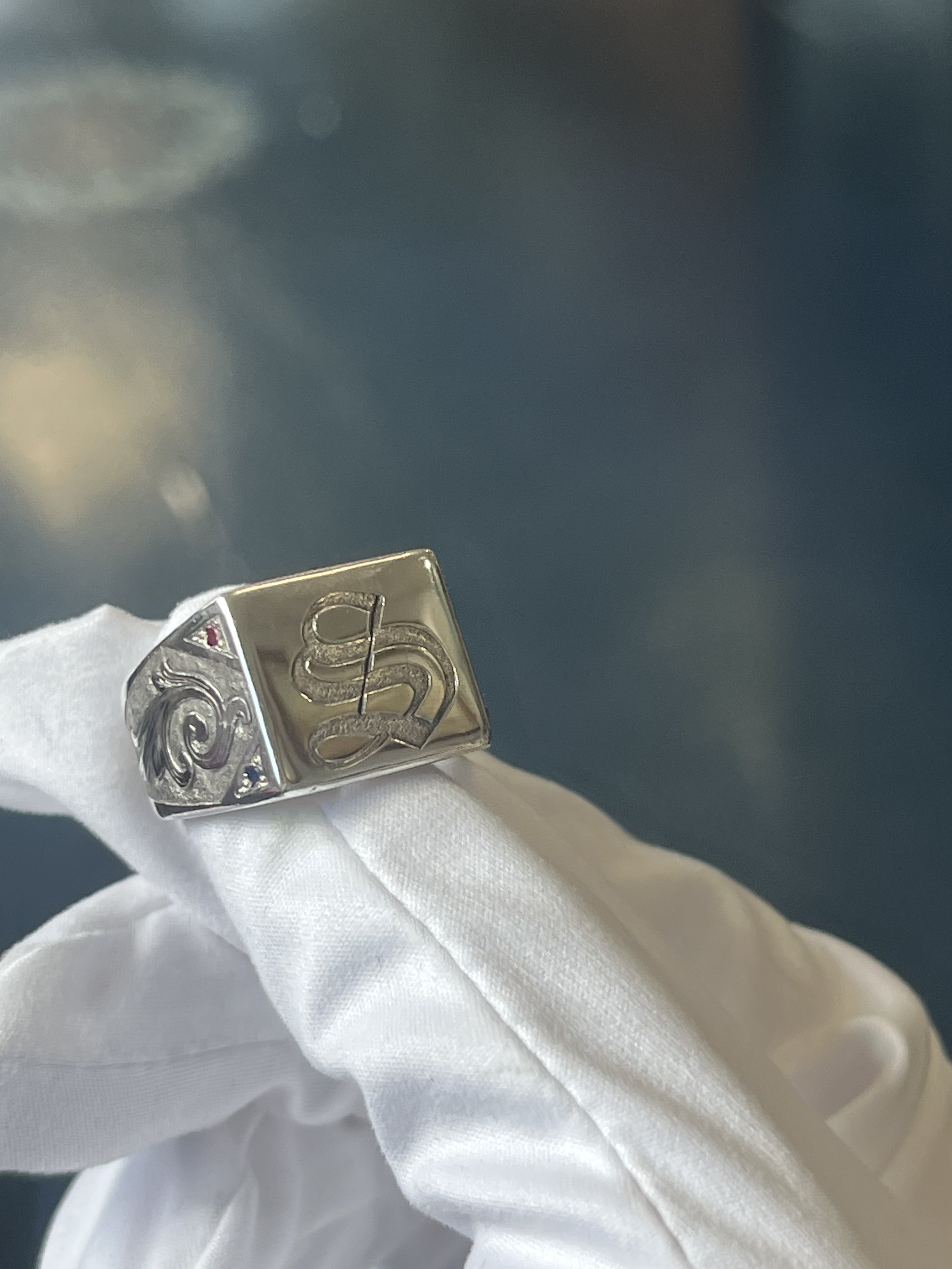 Silver ring with carved design, held by a white-gloved hand against a dark background.