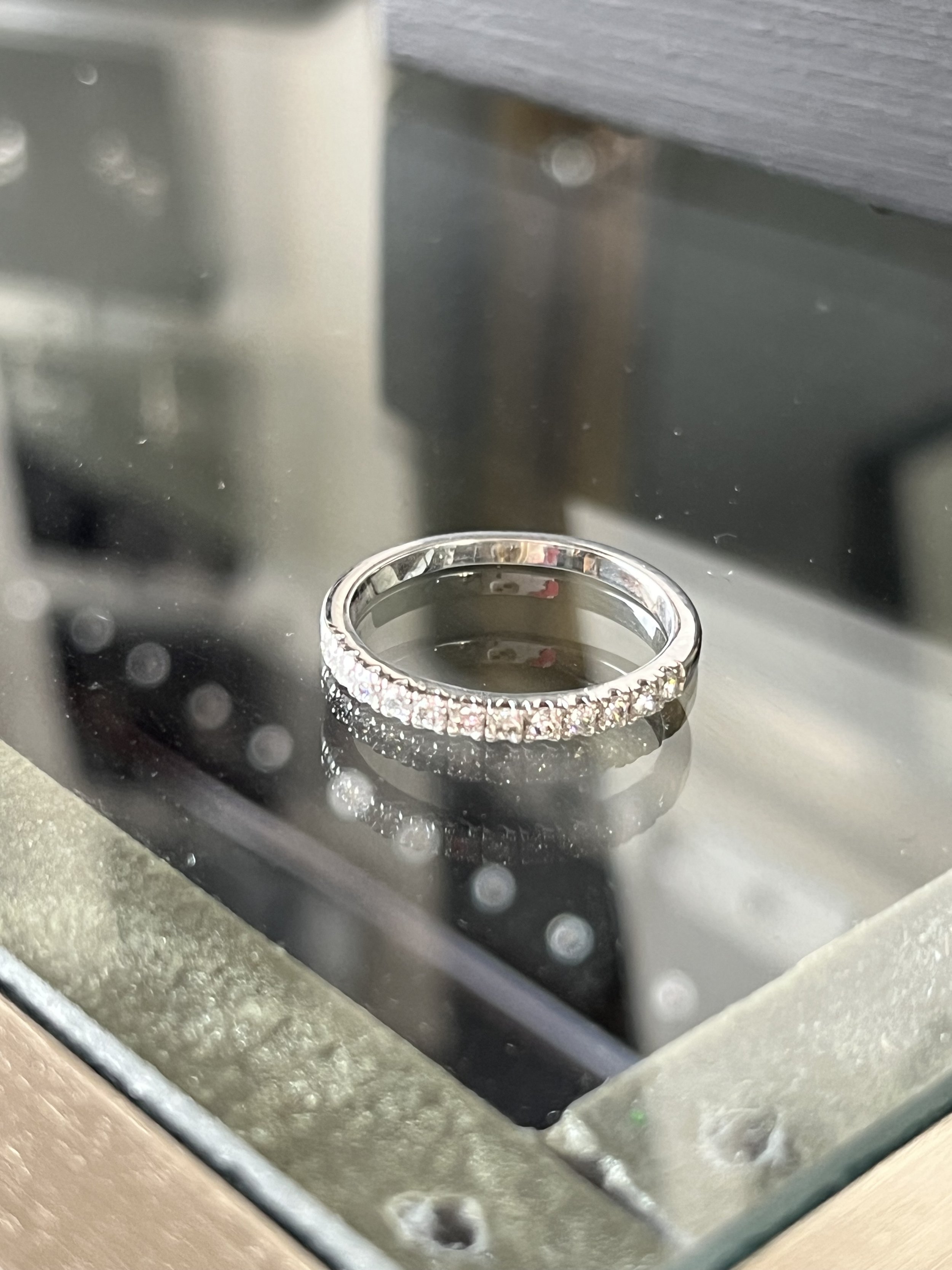 A silver ring with small diamonds displayed inside a glass case.