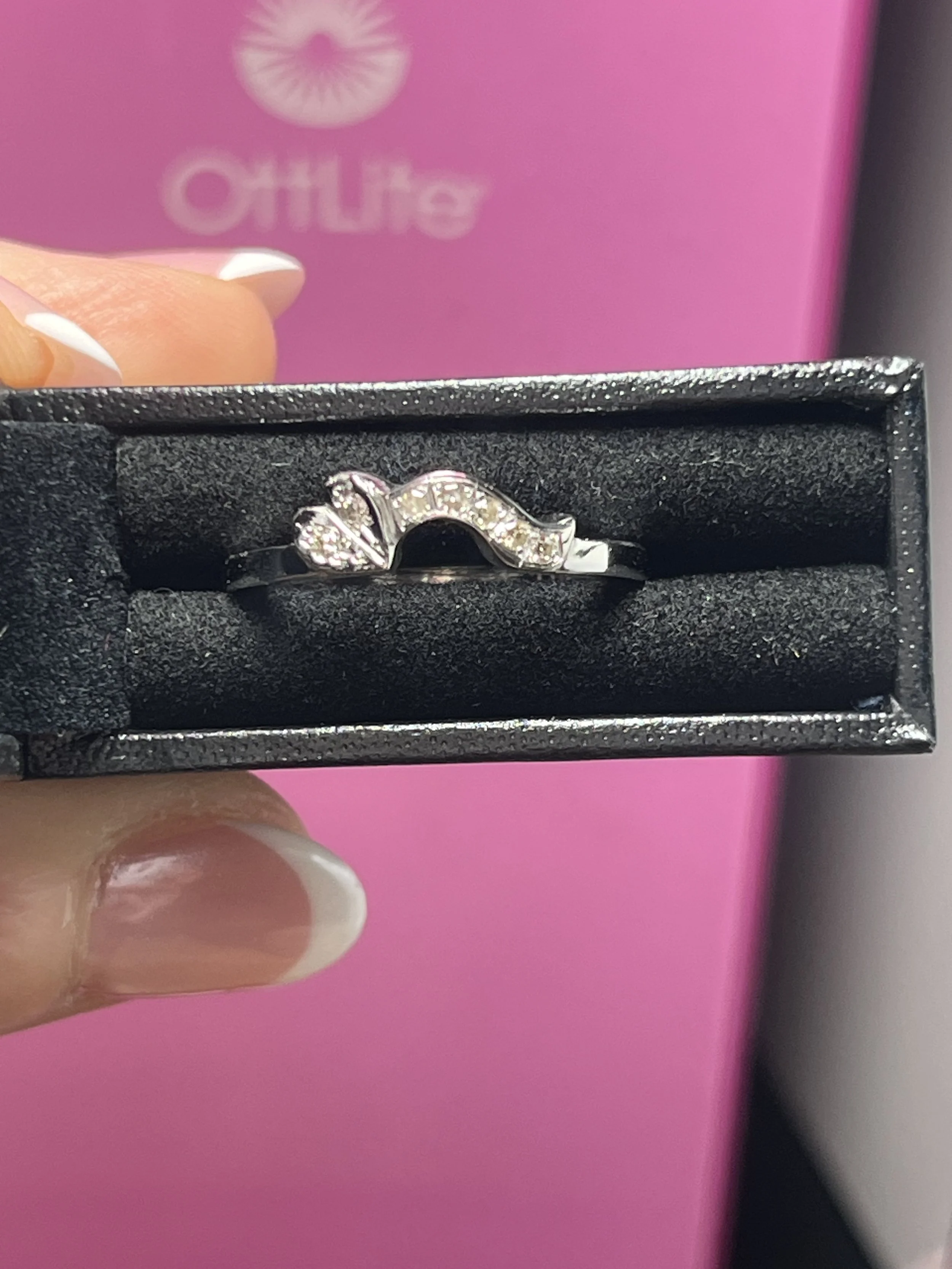 A silver ring with a wave design, decorated with small clear gemstones, inside a black jewelry box.