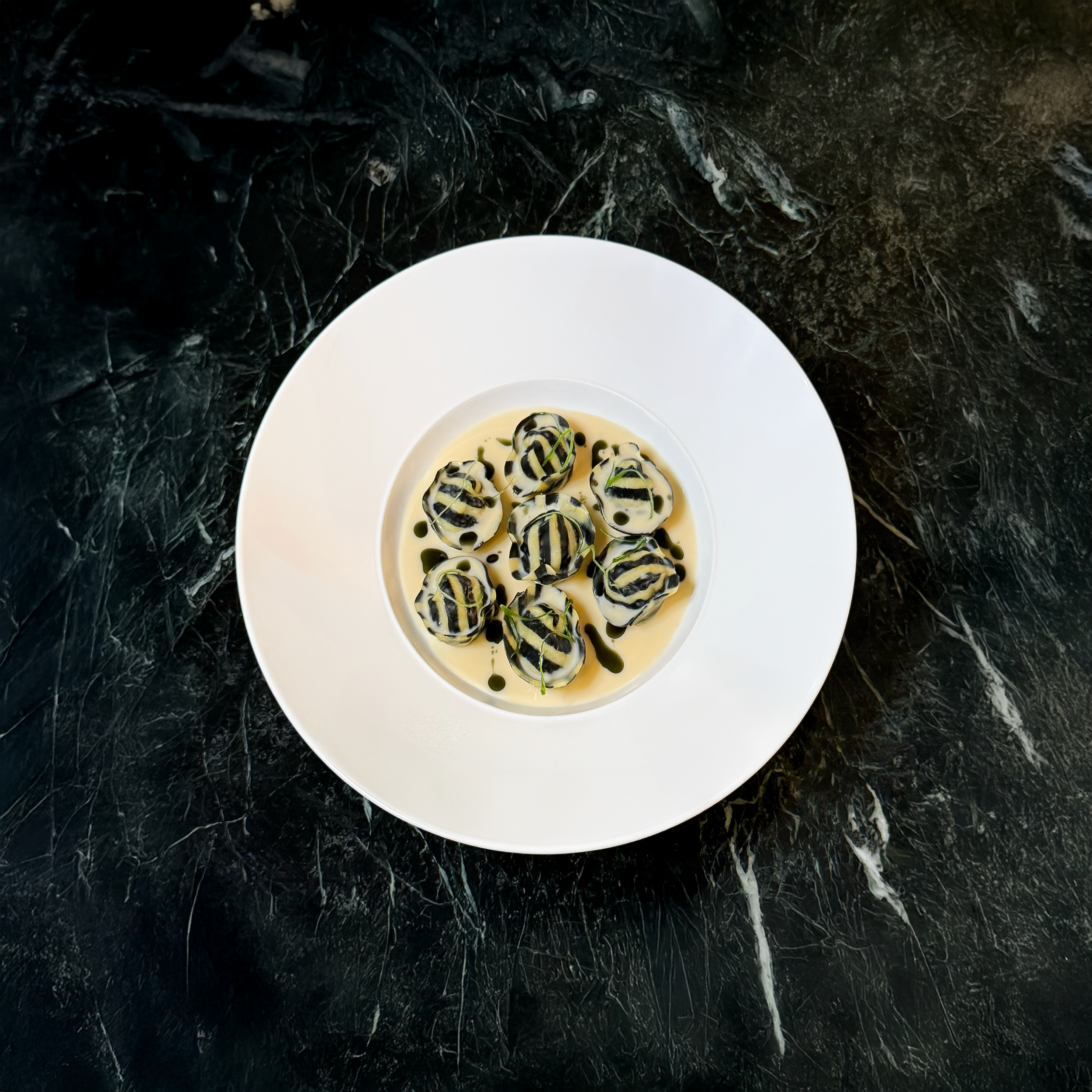 A white plate with striped ravioli topped with balsamic glaze on a dark marble surface.