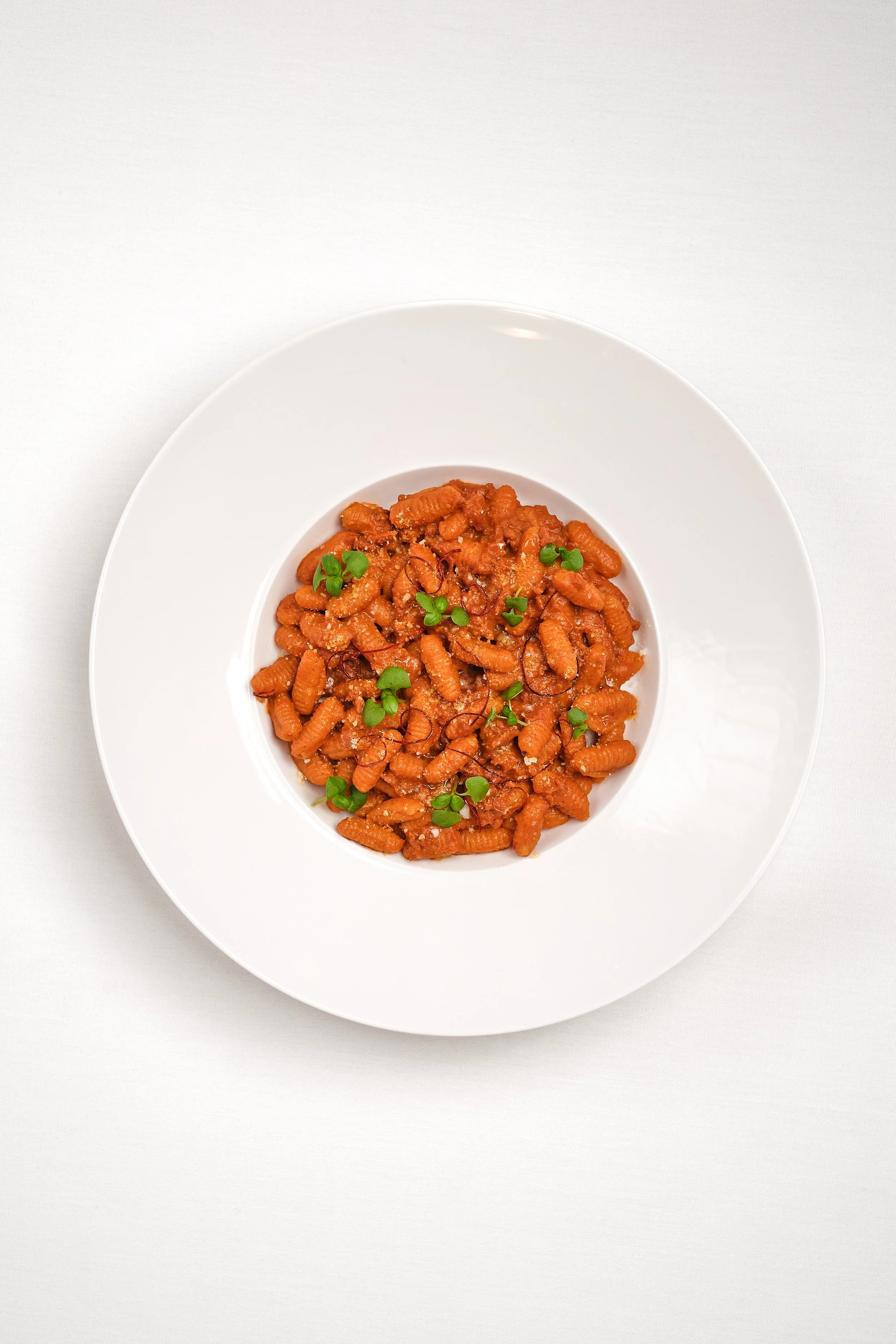 Plate of gnocchi pasta garnished with microgreens on a white background.
