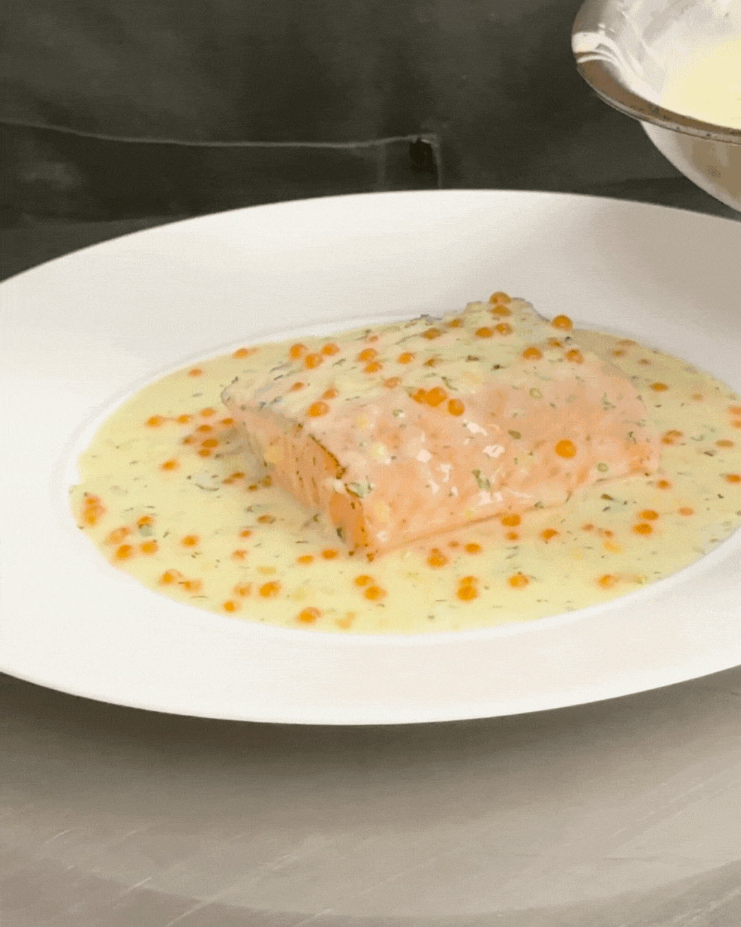 Piece of salmon fish with orange roe, creamy sauce, and herbs on a white plate.