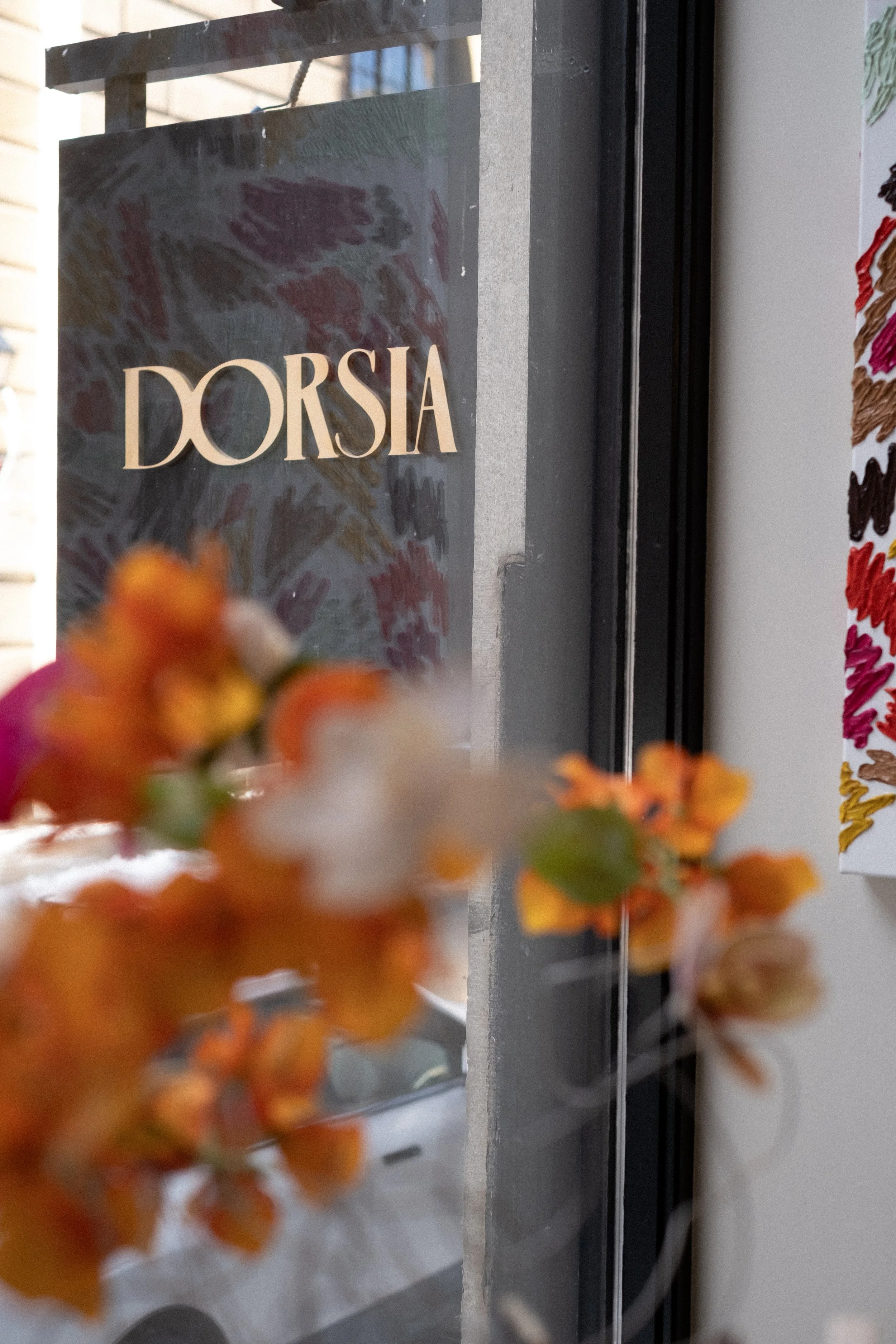 A store sign reading 'DORSIA' seen through orange flowers with a blurred background.