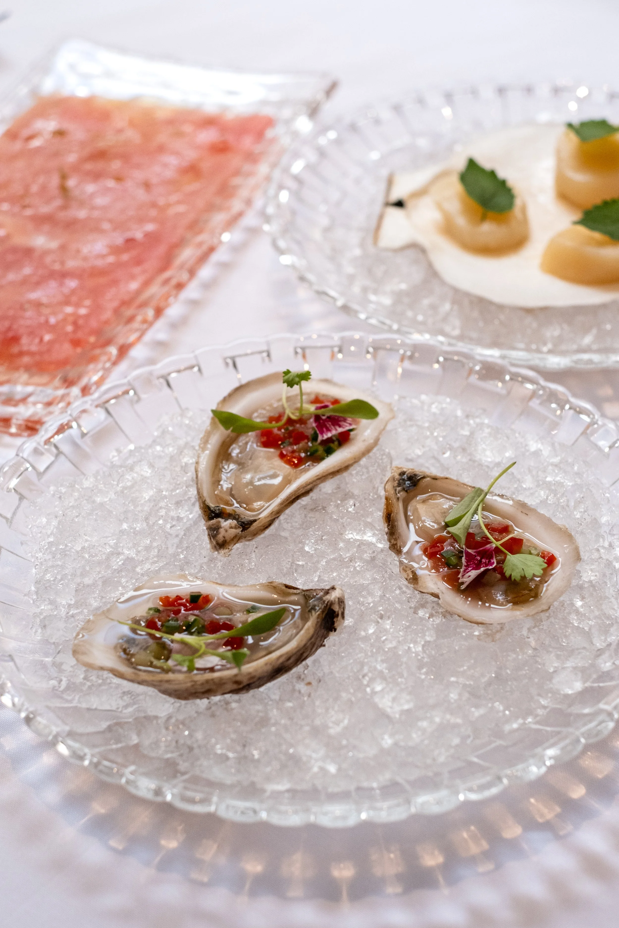 Three raw oysters on a bed of crushed ice garnished with microgreens and red pepper flakes, served on a glass dish.