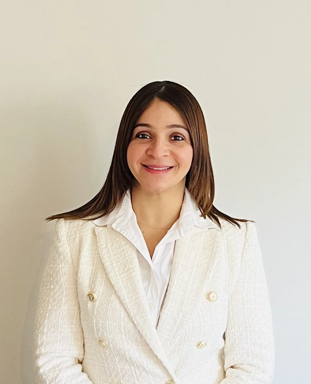 Johanna O'Brien, Counseling Intern, specializing in counseling for individuals and therapy in Spanish. A young woman with shoulder-length brown hair smiling, wearing a blazer over a white shirt, standing against a plain light-colored wall.