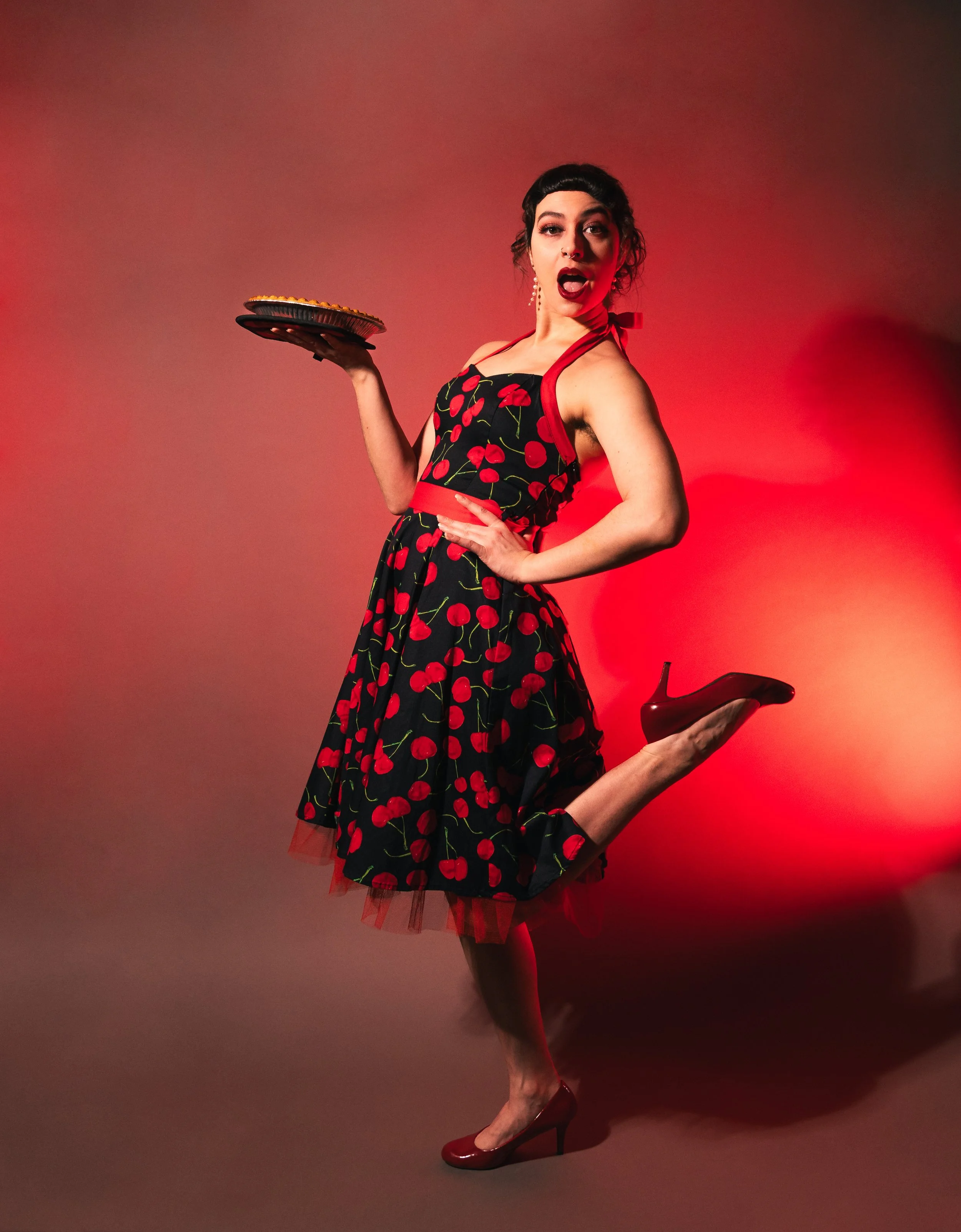 Cherry wears a cherry print dress and holds a pie in her right hand with her left foot popped