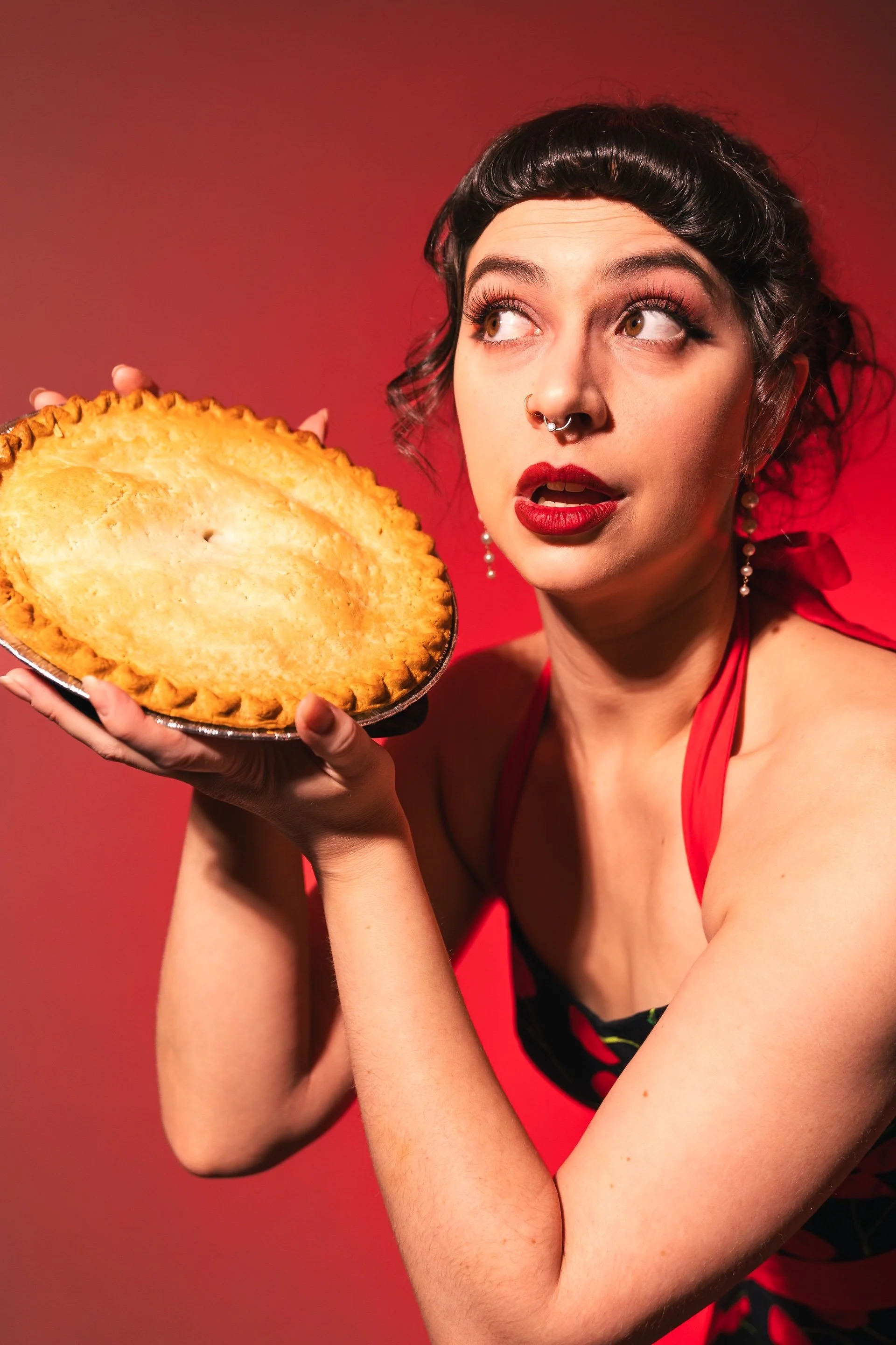 Cherry holds a pie up next to her face and looks off camera