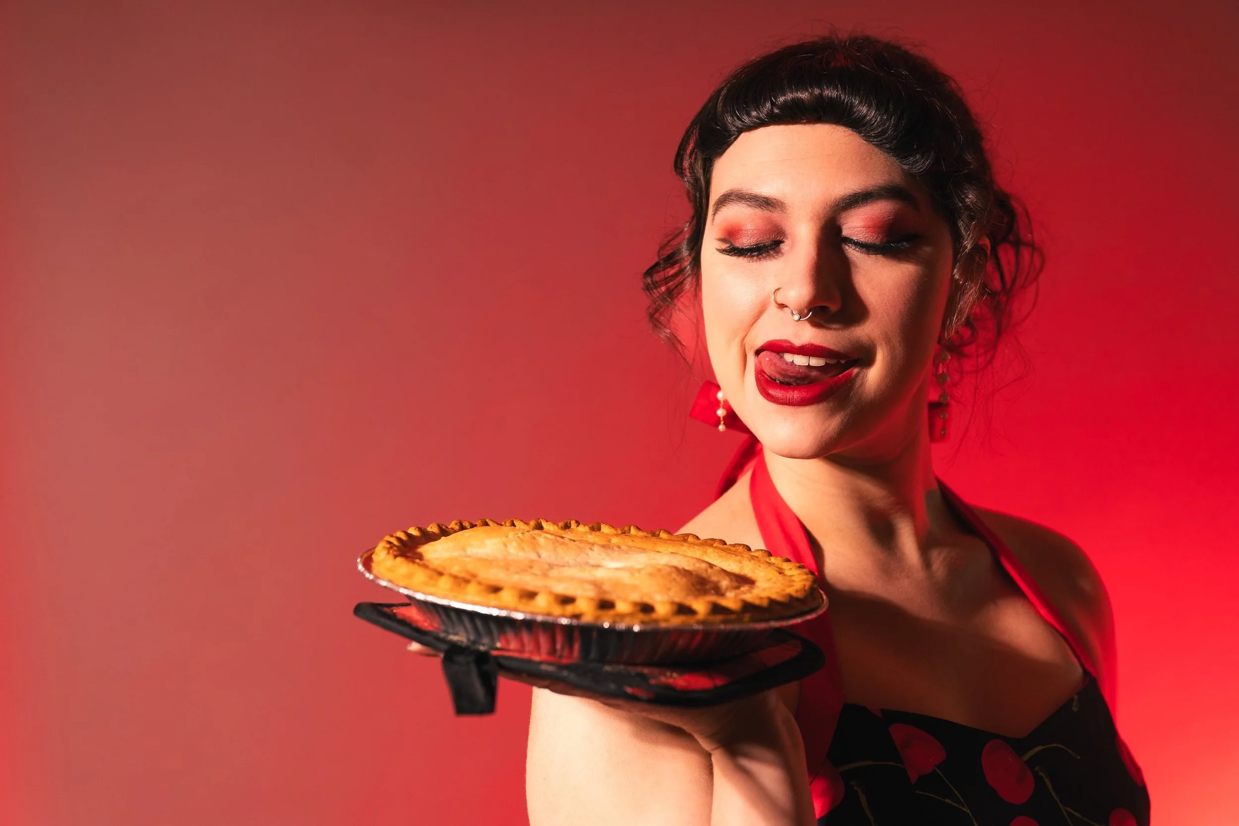 Cherry holds a pie out to the viewer while looking down at it and licking her lips
