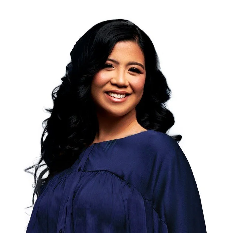 A smiling woman with long black hair in loose curls, wearing a navy blue dress, against a plain white background.
