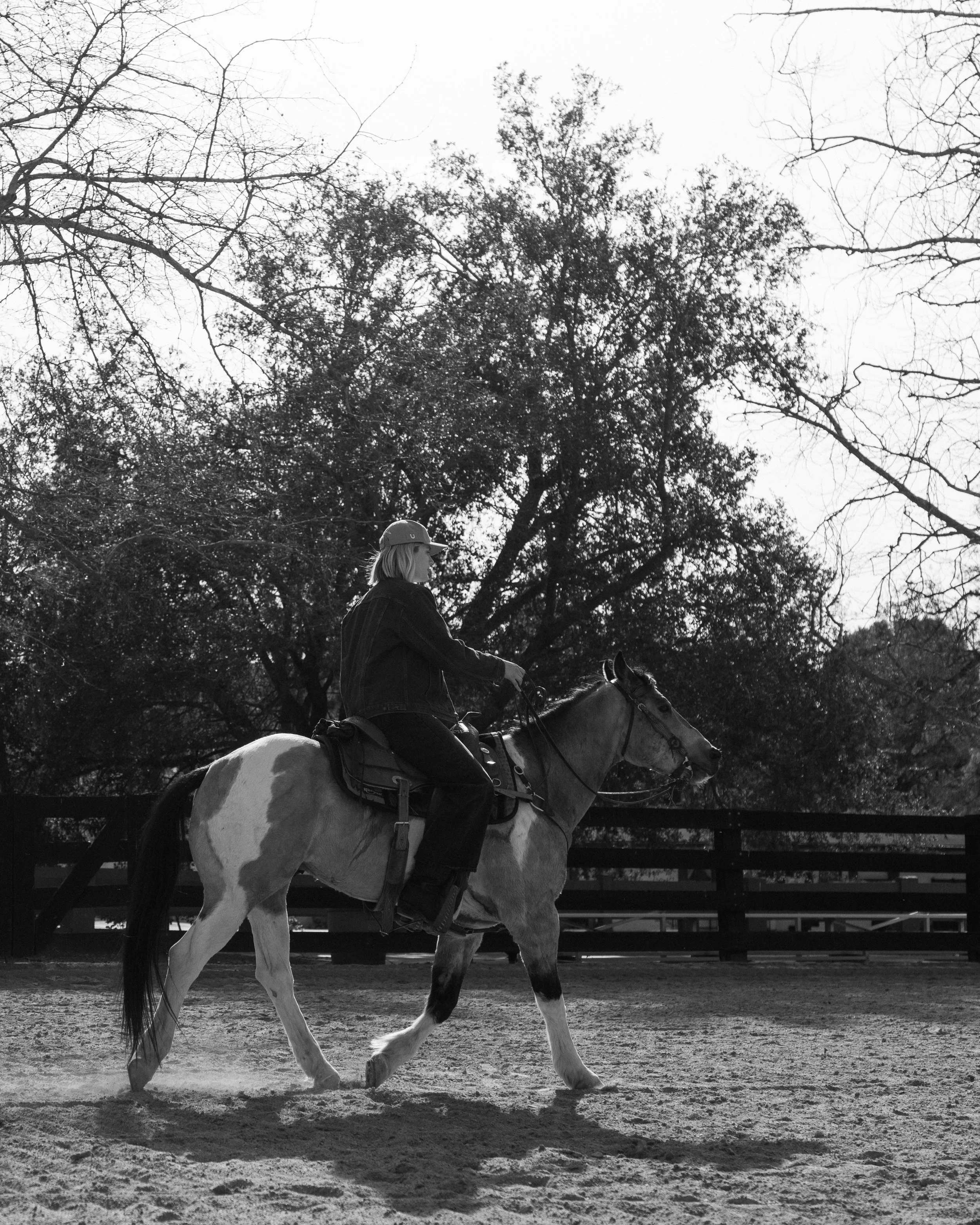 A woman riding a horse in an outdoor arena with trees in the background.
