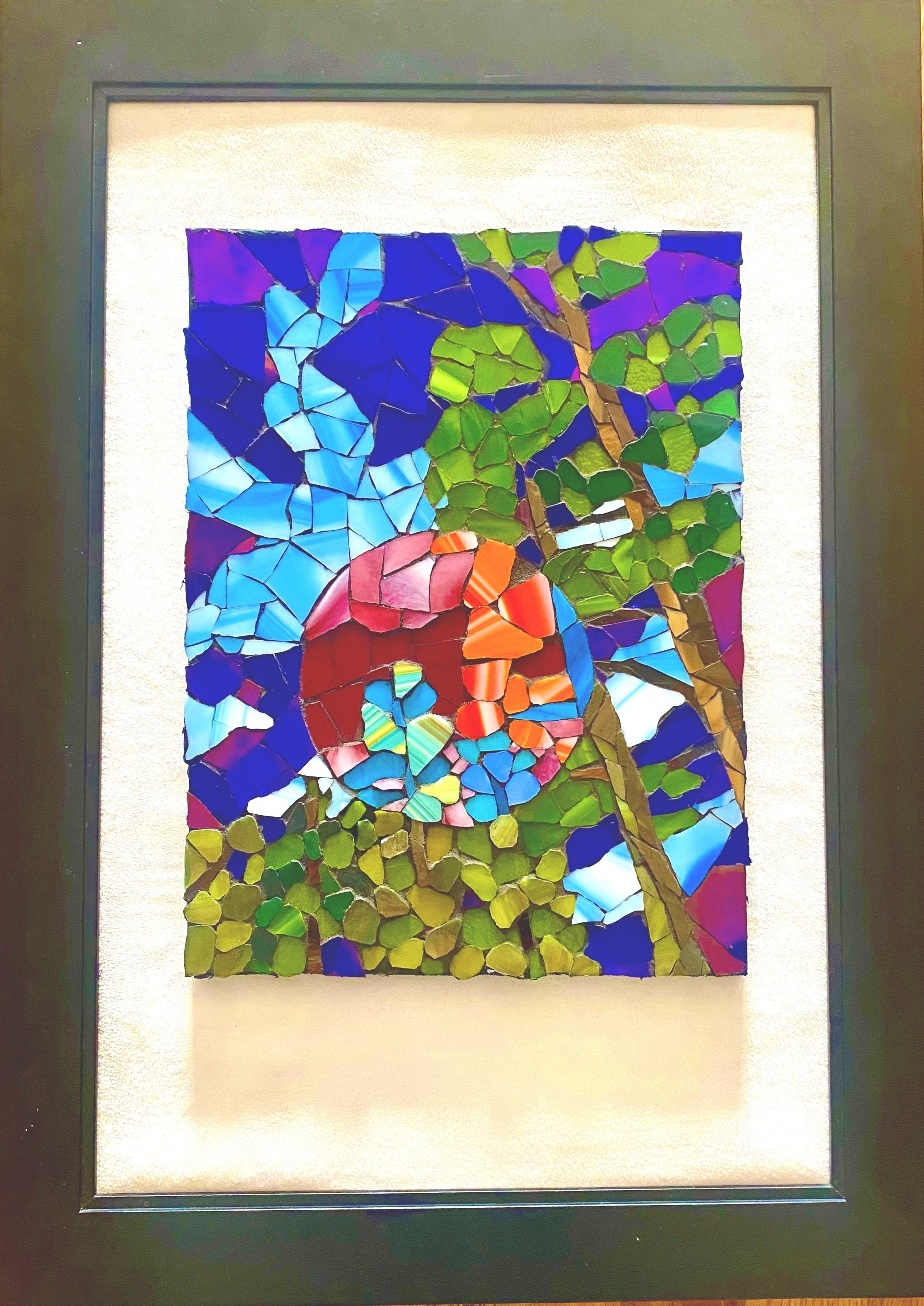 Glass mosaic of tall trees with green leaves set against a vibrant blue sky, featuring a large red and multicolored circular shape in the center