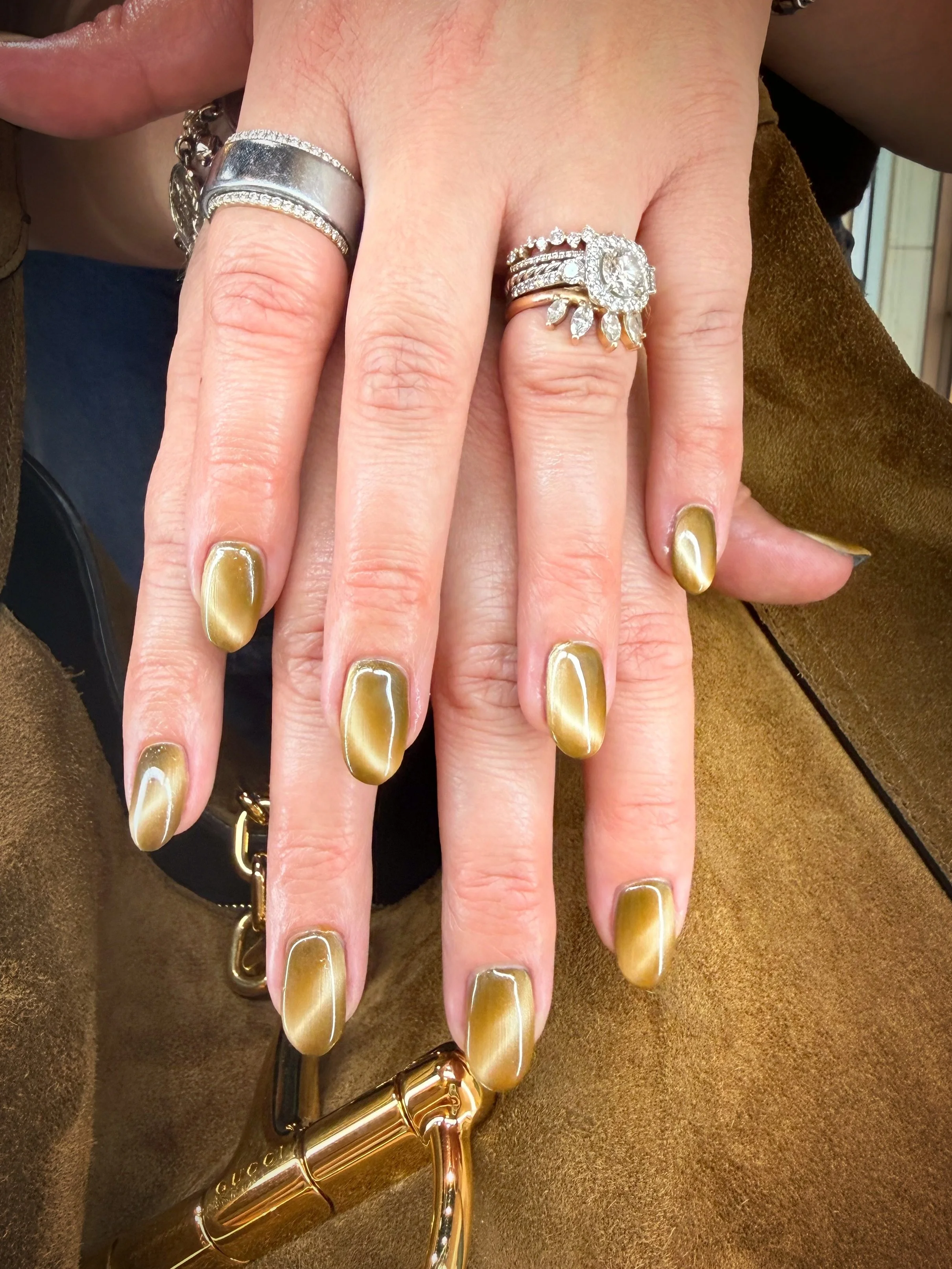 Close-up of hands with gold and silver rings and gold metallic nail polish, holding a gold lipstick case.