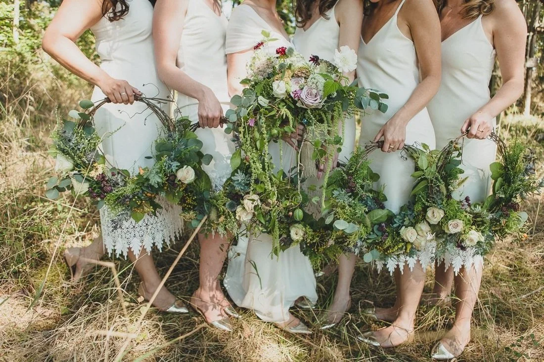 Group of women in white dresses holding floral hoops outdoors. Local flowers, wedding orcas island. Bridesmaid's hoop, wreath.