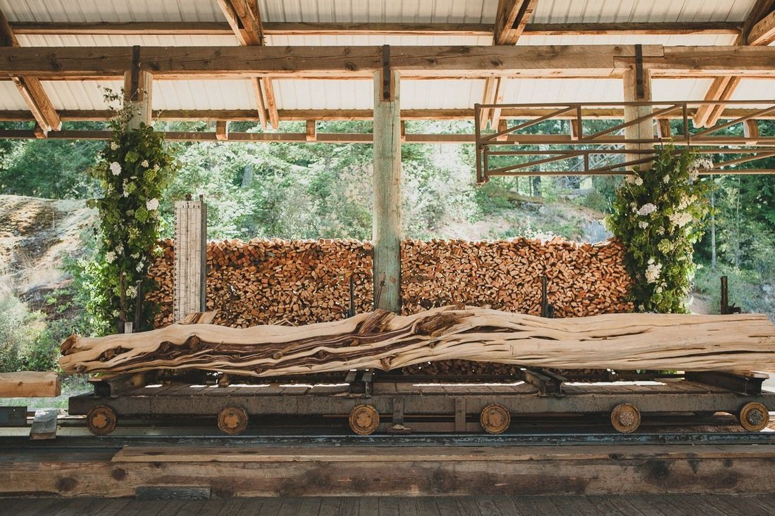 Sawmill wedding, Orcas Island, Turtleback Farm, venue, wedding. Large, twisted wooden log on a moving tram, with stacks of chopped firewood and greenery in the background.