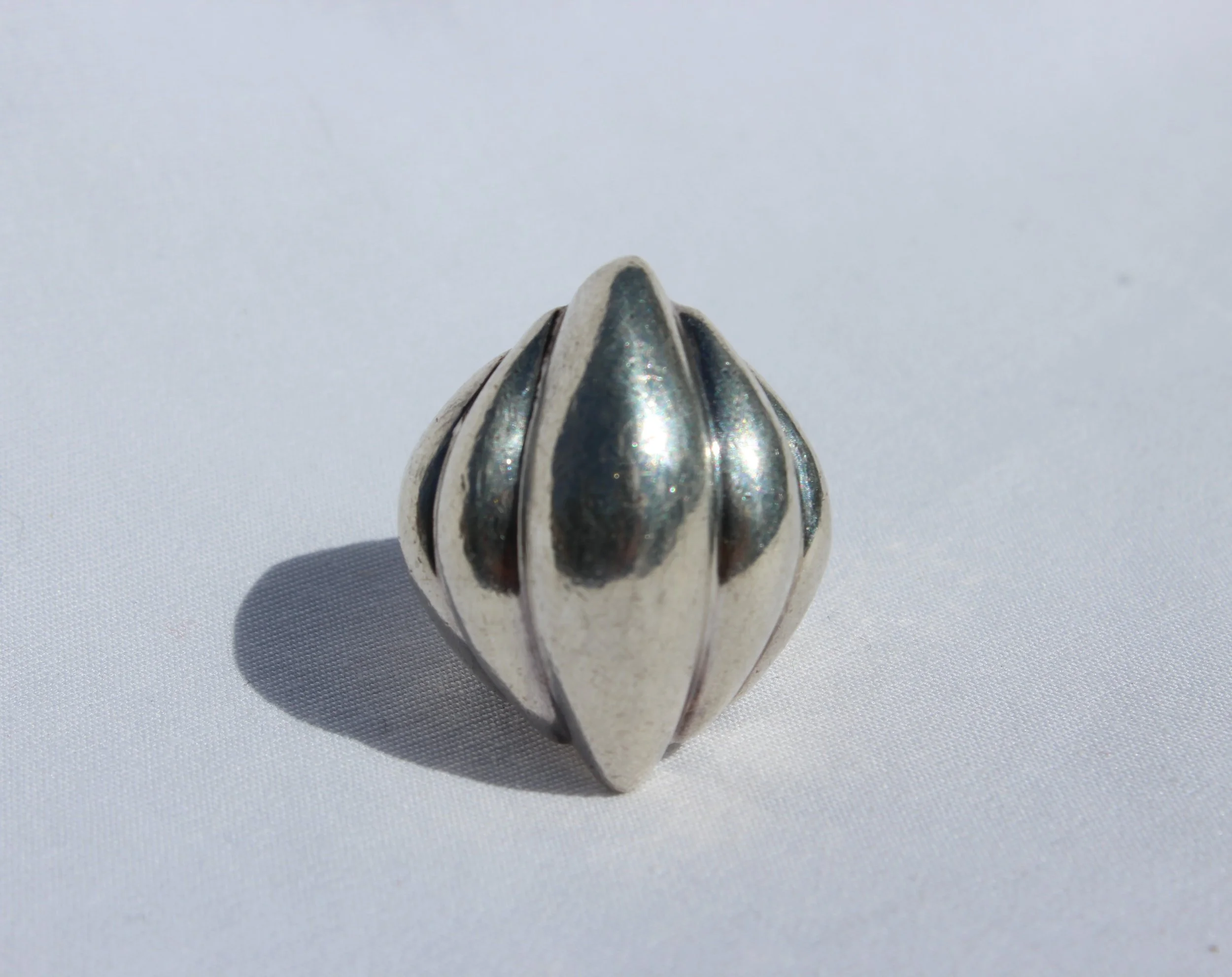 A chunky silver ring with a fluted design, casting a shadow on a white background.