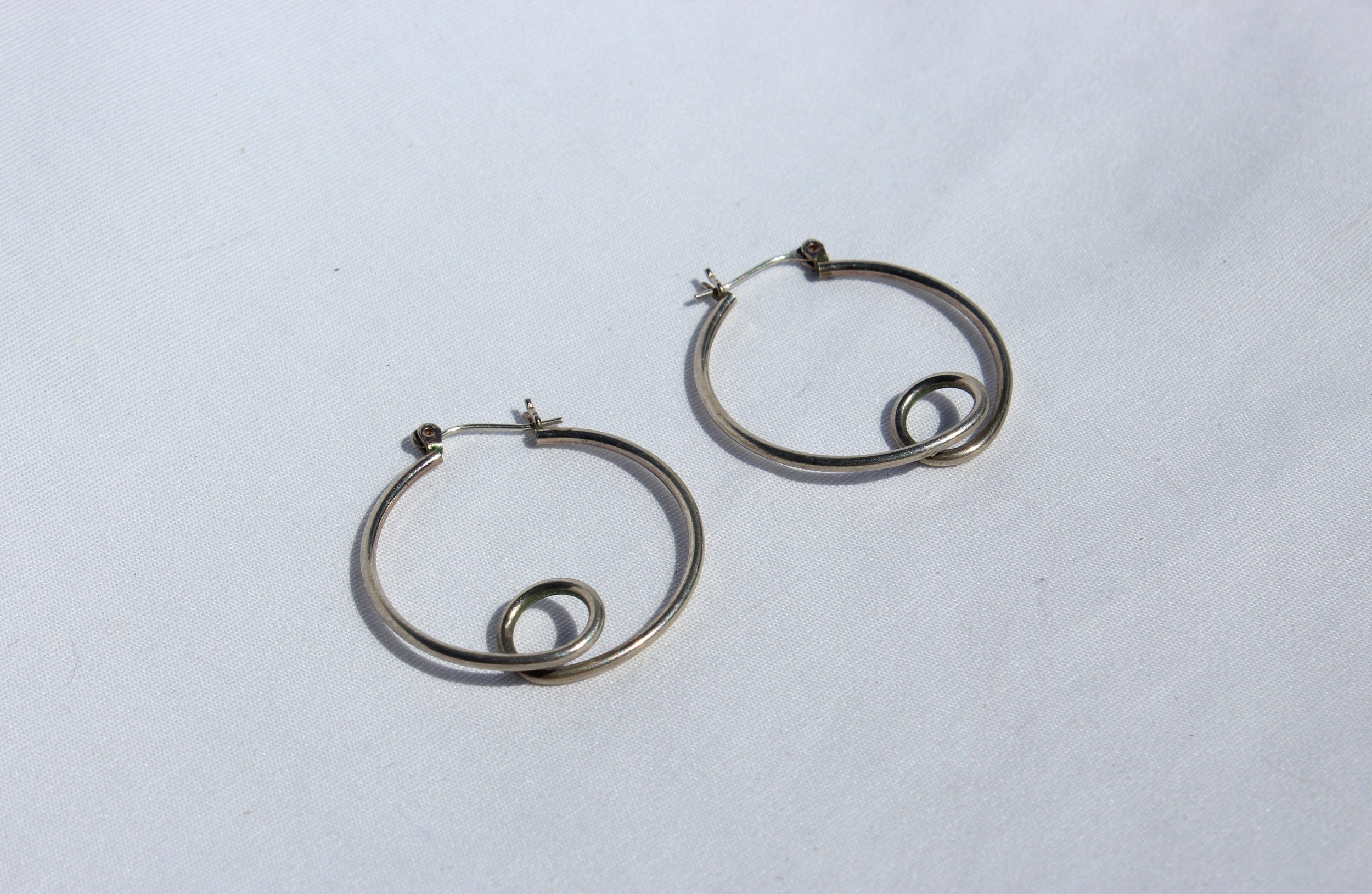 A pair of silver hoop earrings with a small spiral design inside each hoop, placed on a plain white background.