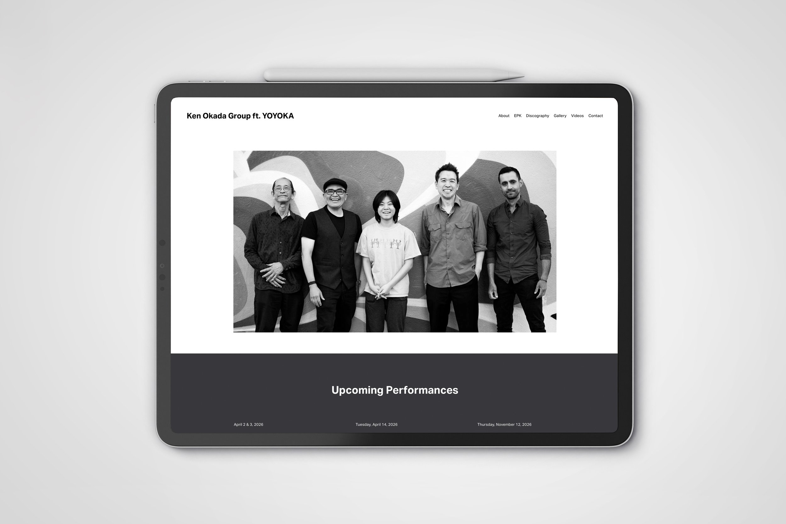 Black-and-white photograph of five people standing in front of a mural, smiling, with a festival or event schedule below. The schedule includes dates in April and November 2026.