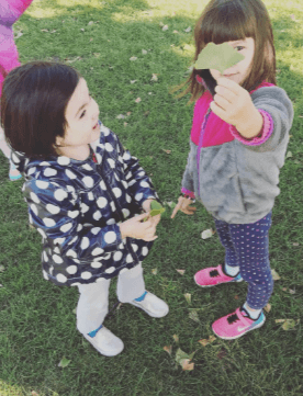 two little girls in the grass holding up fallen leaves