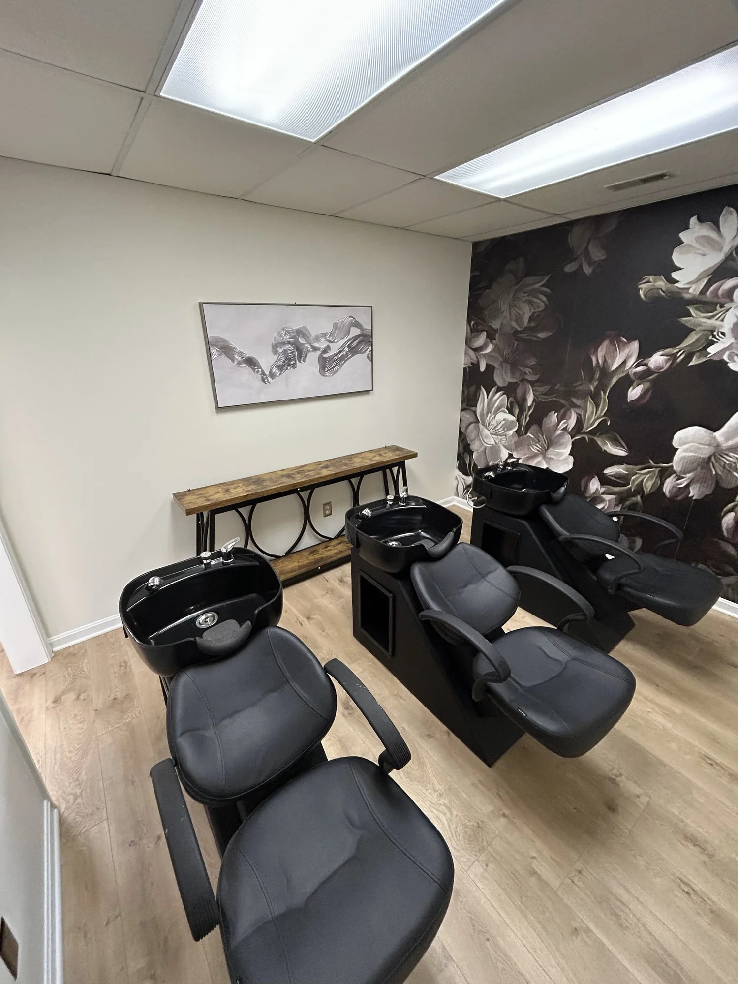 Wash bowl room with three black shampoo stations and a dark floral mural